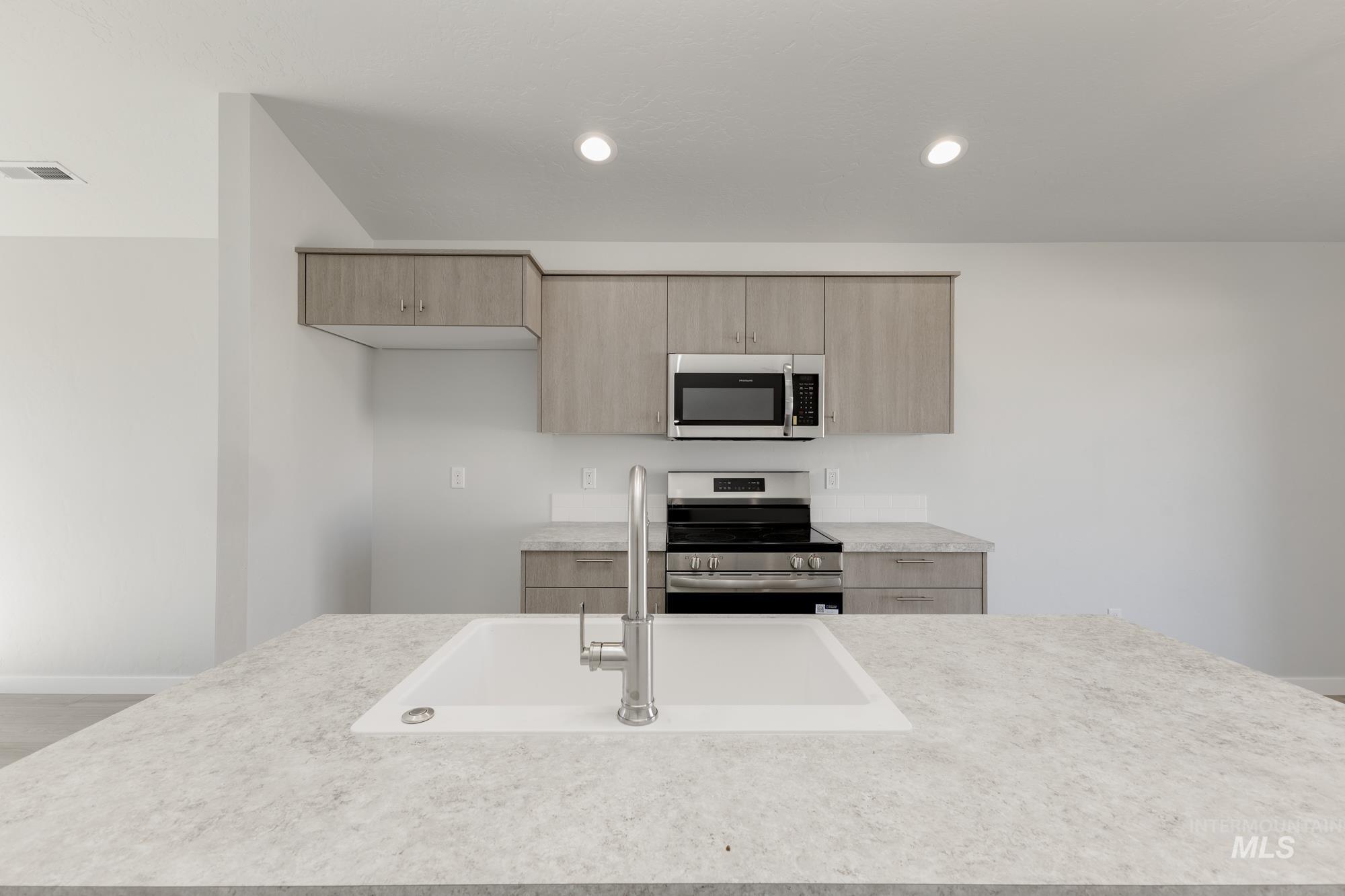 Kitchen featuring appliances with stainless steel finishes, modern cabinets, light brown cabinetry, recessed lighting, and light stone counters