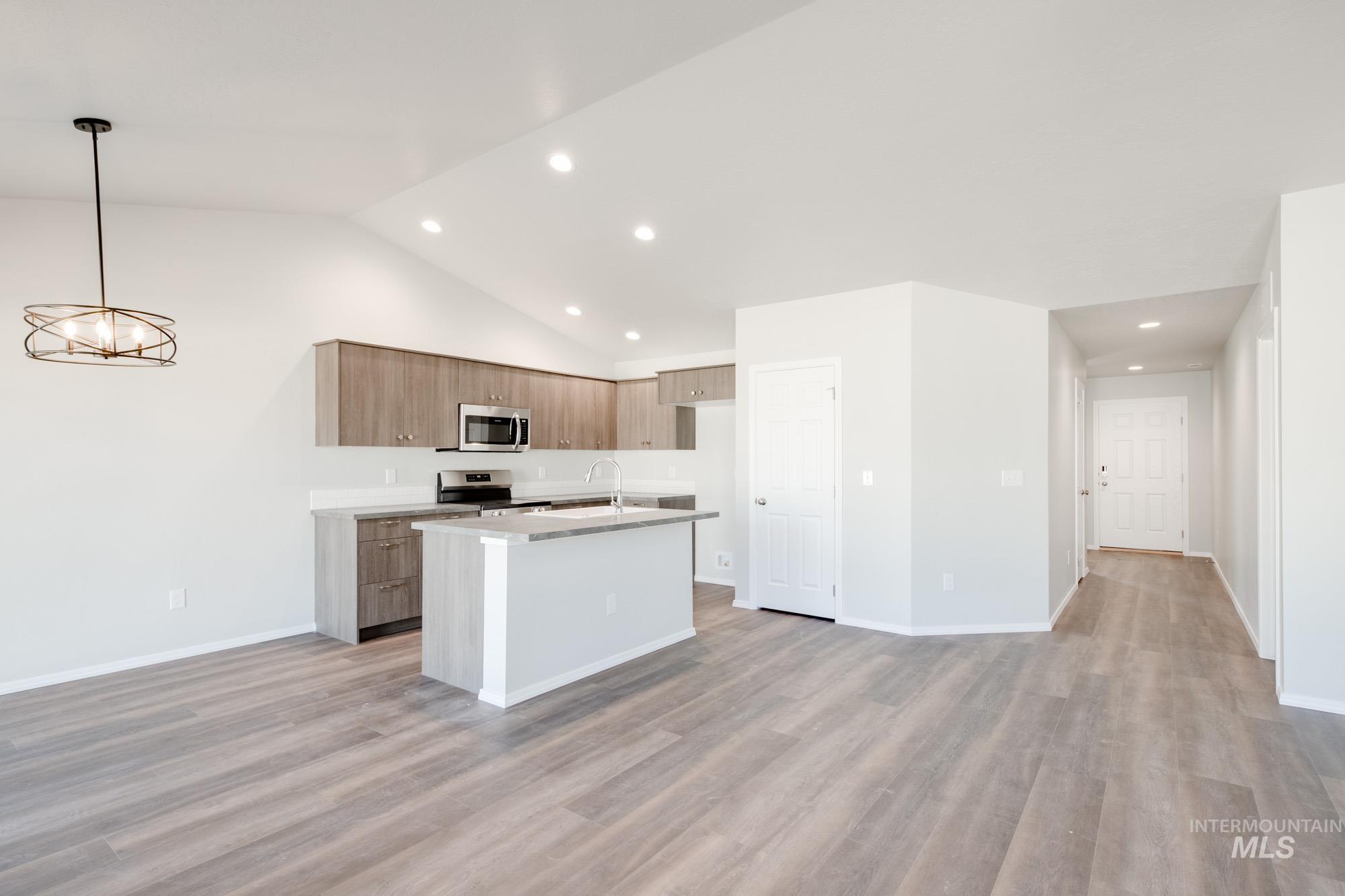 Kitchen with an island with sink, light wood finished floors, hanging light fixtures, recessed lighting, and open floor plan