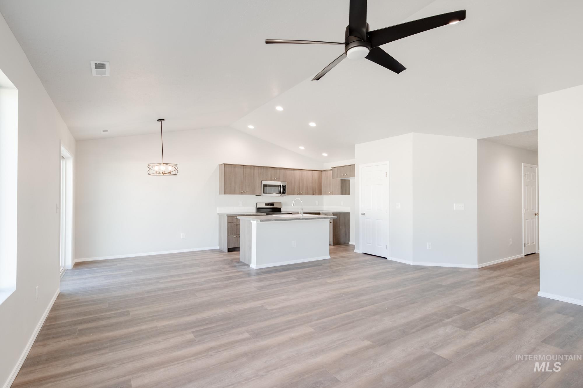 Unfurnished living room with light wood finished floors, a ceiling fan, recessed lighting, a chandelier, and high vaulted ceiling