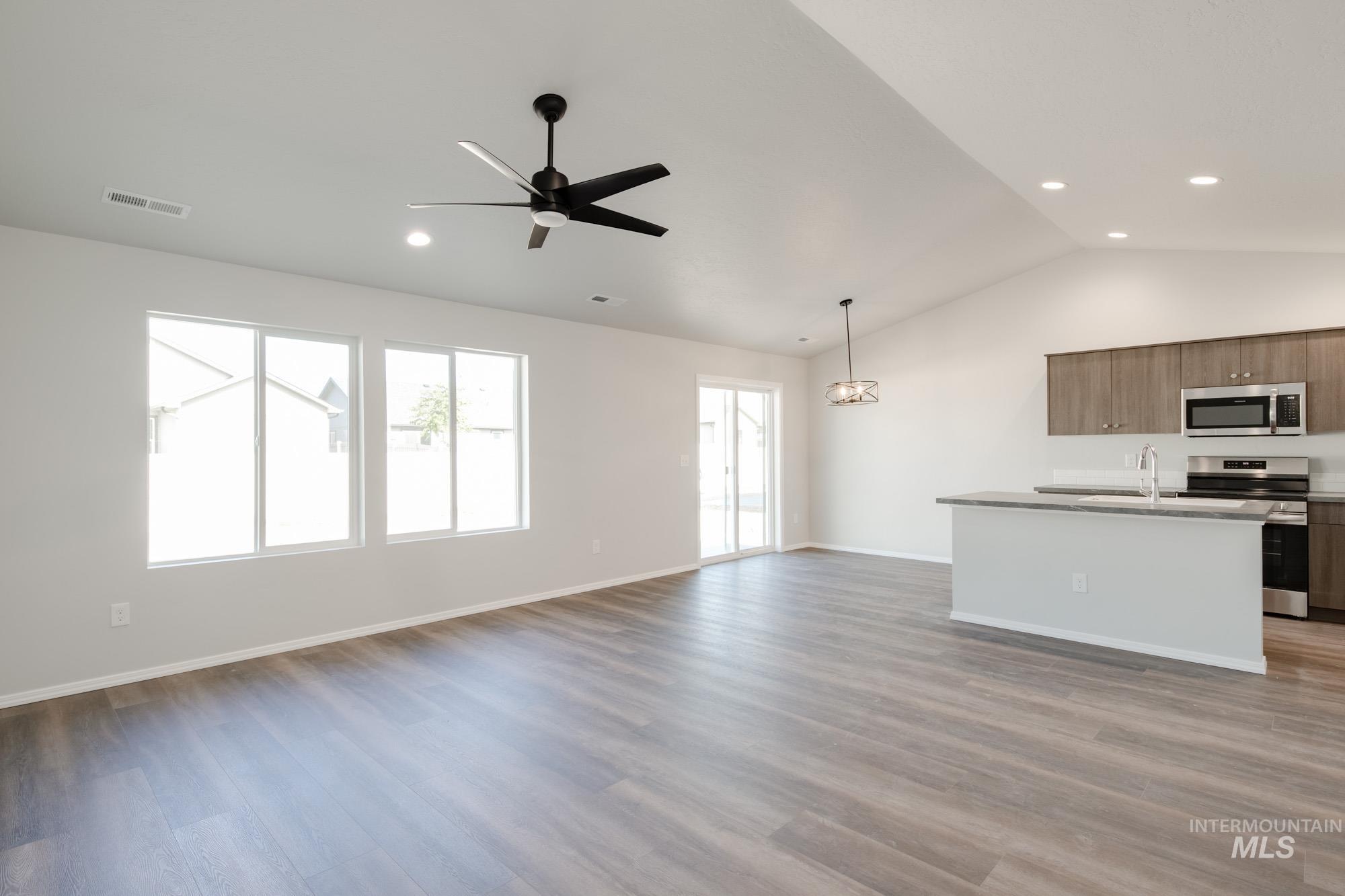 Kitchen with open floor plan, a kitchen island with sink, lofted ceiling, appliances with stainless steel finishes, and light wood-style flooring