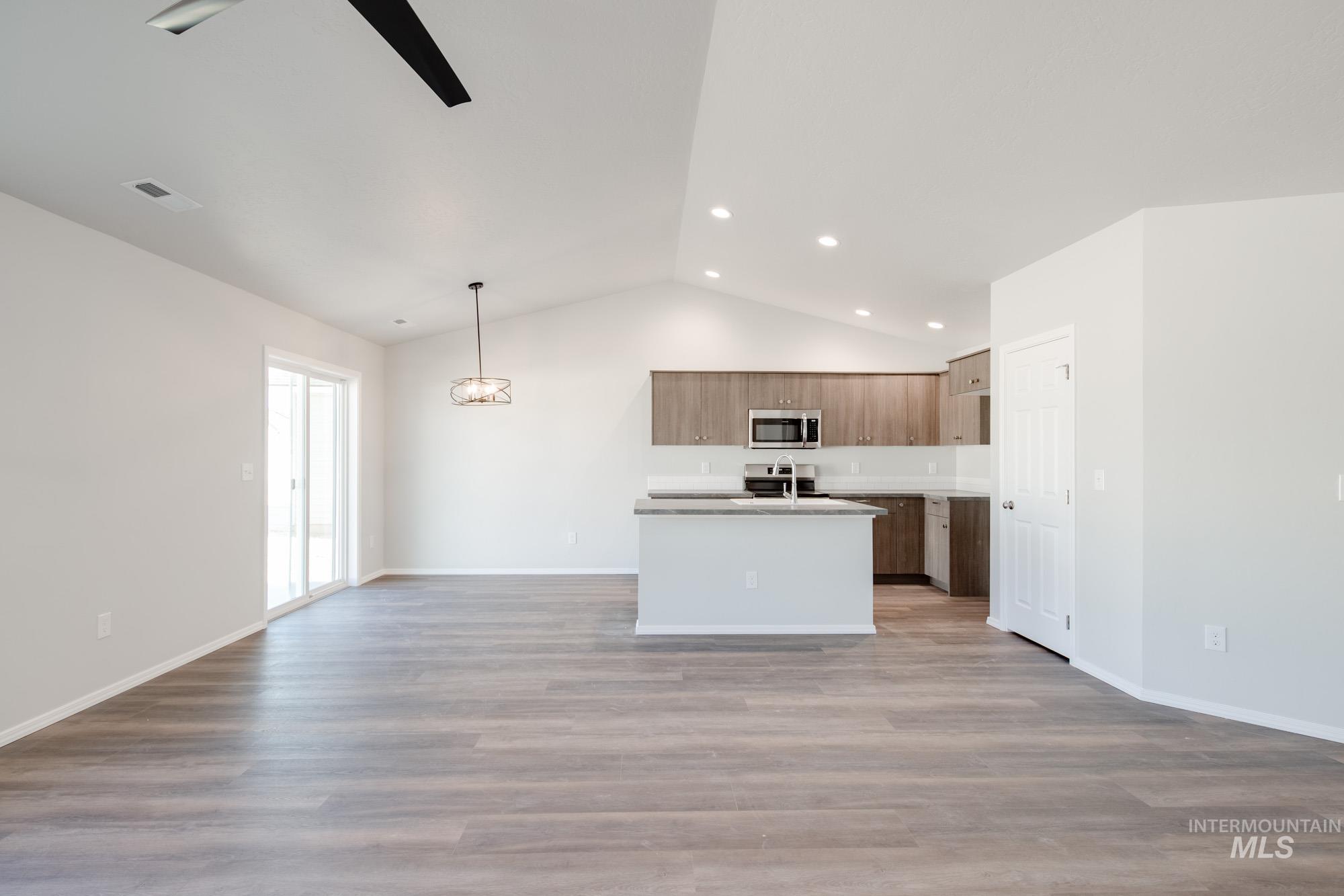 Kitchen with open floor plan, vaulted ceiling, a center island with sink, hanging light fixtures, and light wood-style floors