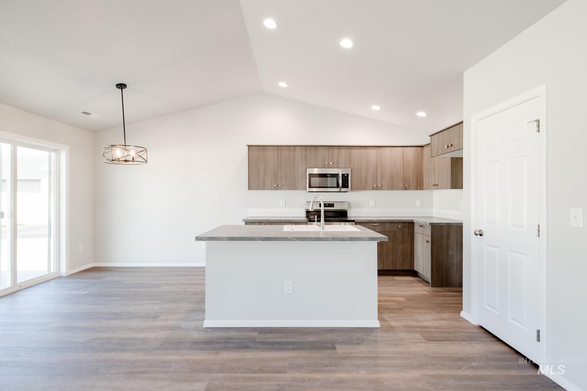 Kitchen featuring a center island with sink, lofted ceiling, light wood-type flooring, modern cabinets, and decorative light fixtures