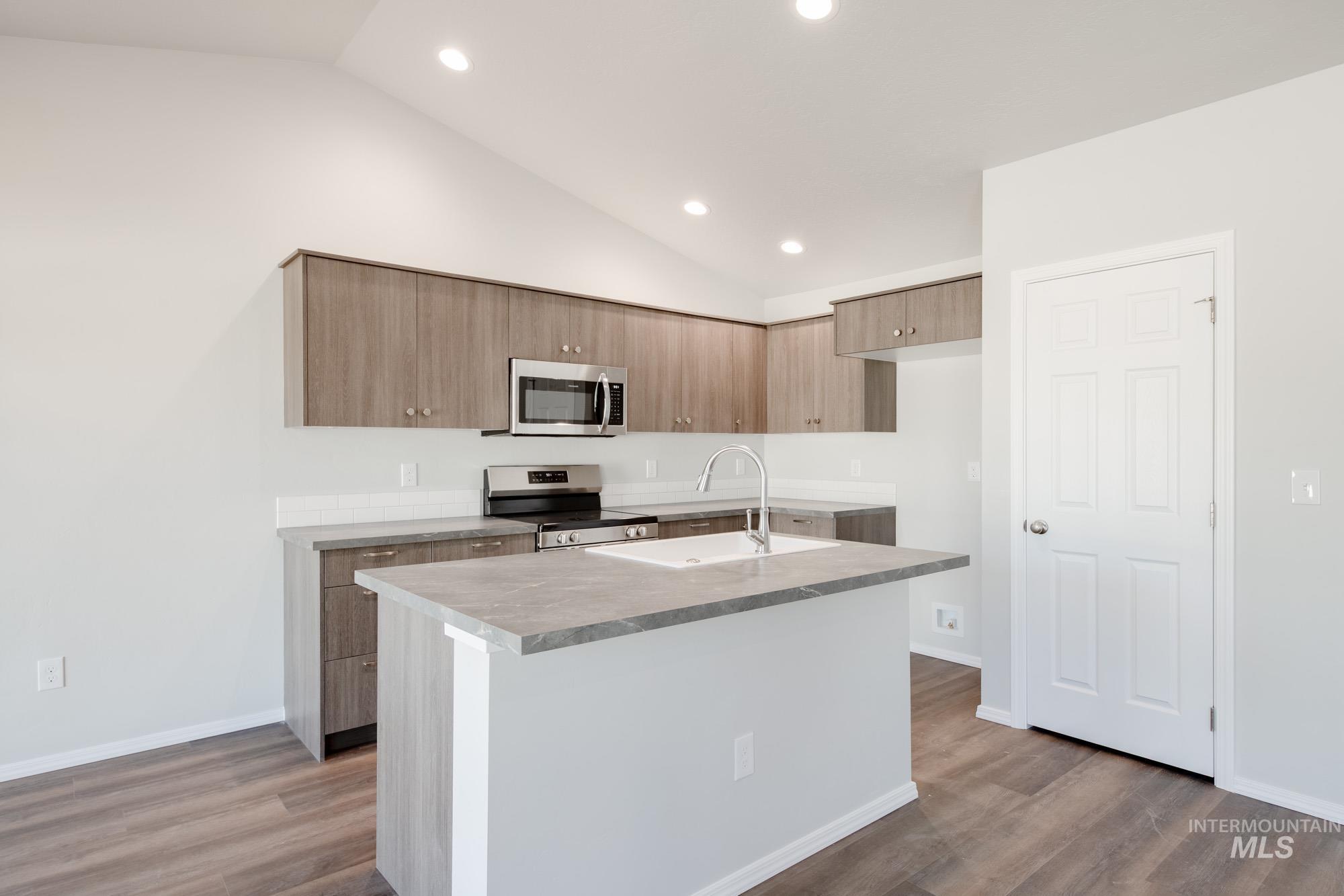 Kitchen with stainless steel appliances, an island with sink, modern cabinets, light wood-type flooring, and light countertops