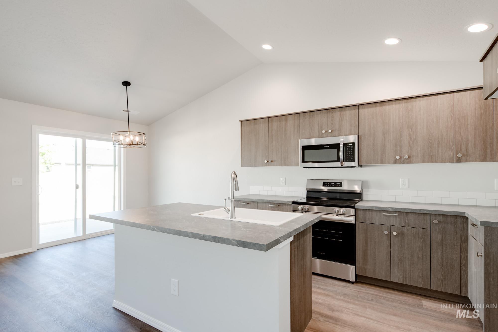 Kitchen featuring stainless steel appliances, vaulted ceiling, light wood-style floors, decorative light fixtures, and a center island with sink