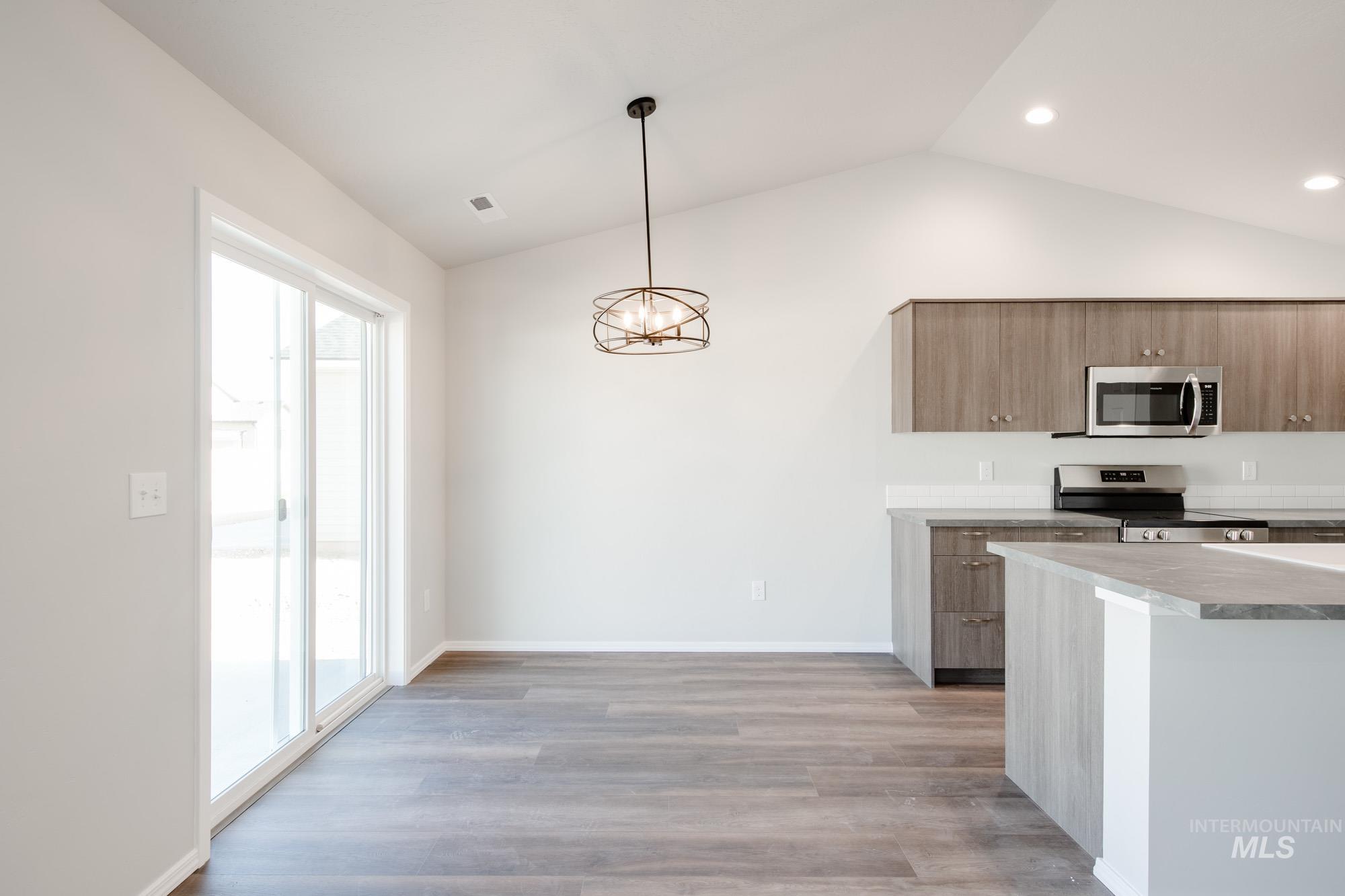 Kitchen featuring light countertops, stainless steel appliances, a chandelier, pendant lighting, and vaulted ceiling