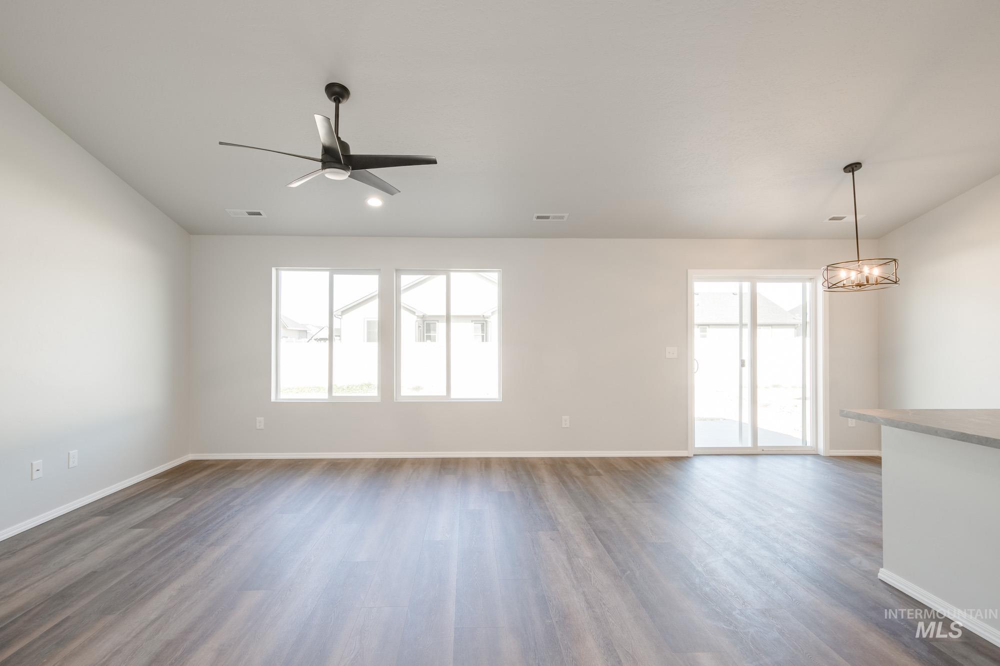 Unfurnished living room featuring dark wood-style flooring, a chandelier, and ceiling fan