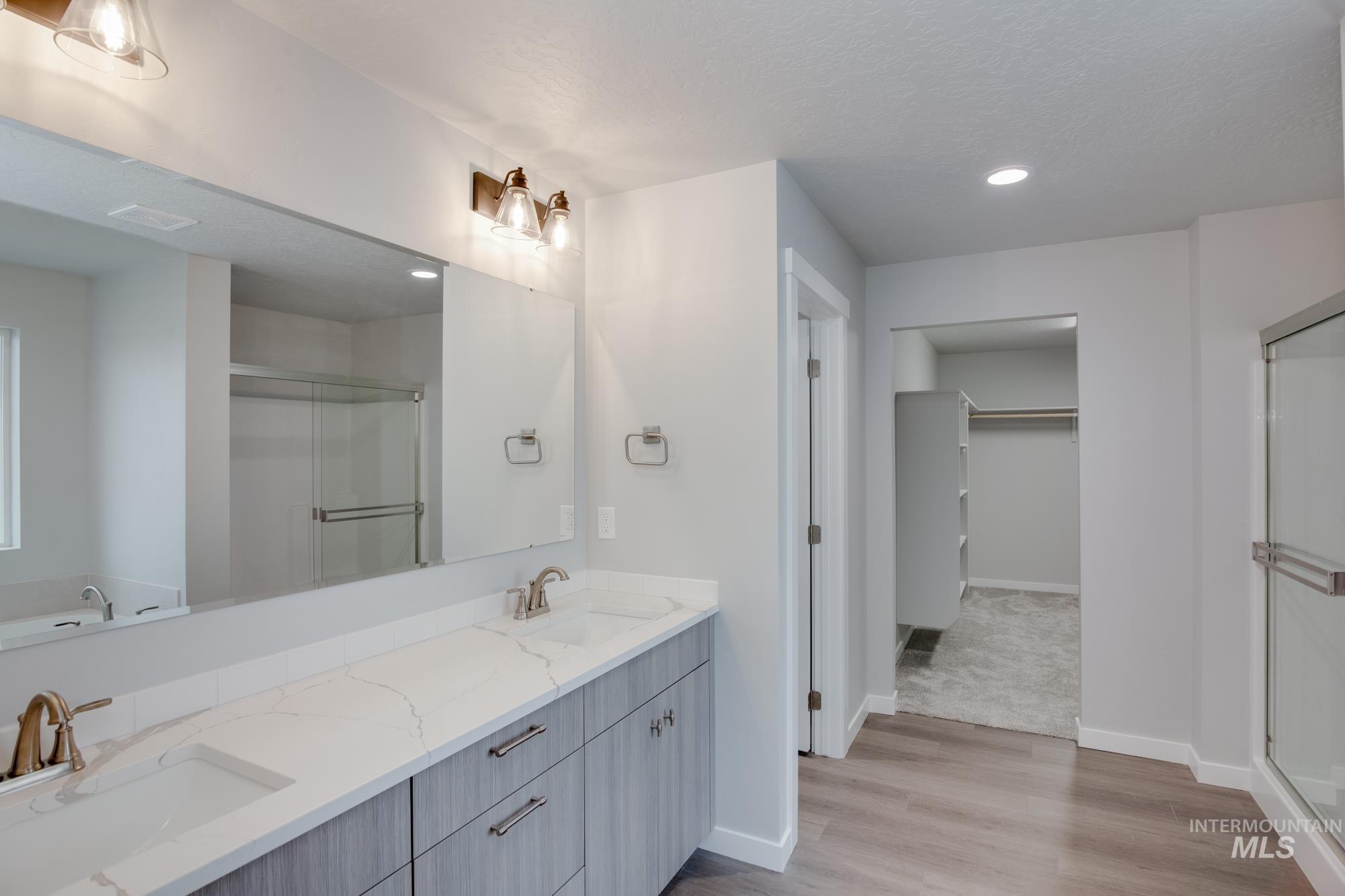 Bathroom with a stall shower, double vanity, a spacious closet, light wood-style floors, and recessed lighting