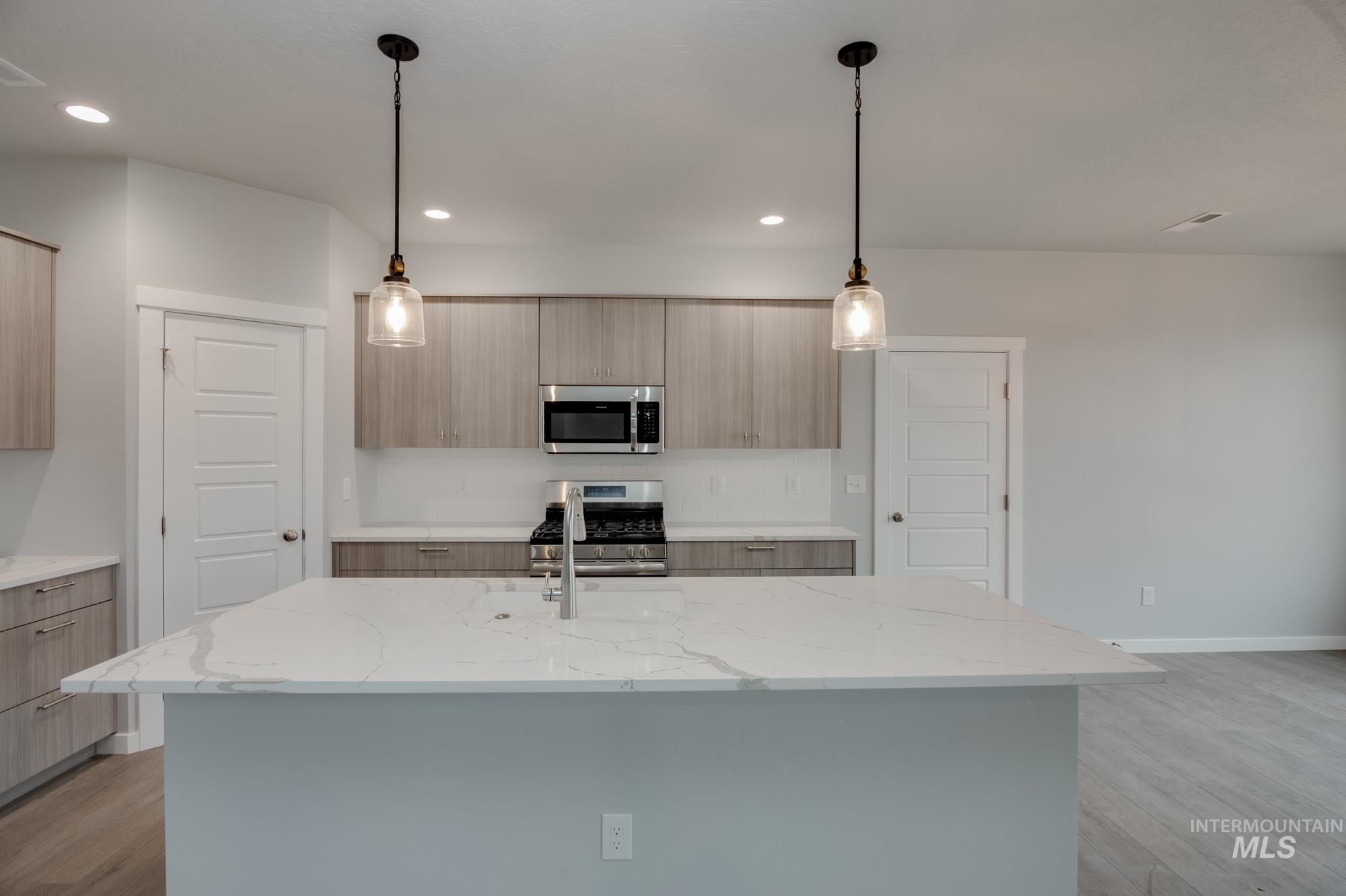 Kitchen featuring light stone counters, light wood-style flooring, appliances with stainless steel finishes, pendant lighting, and modern cabinets
