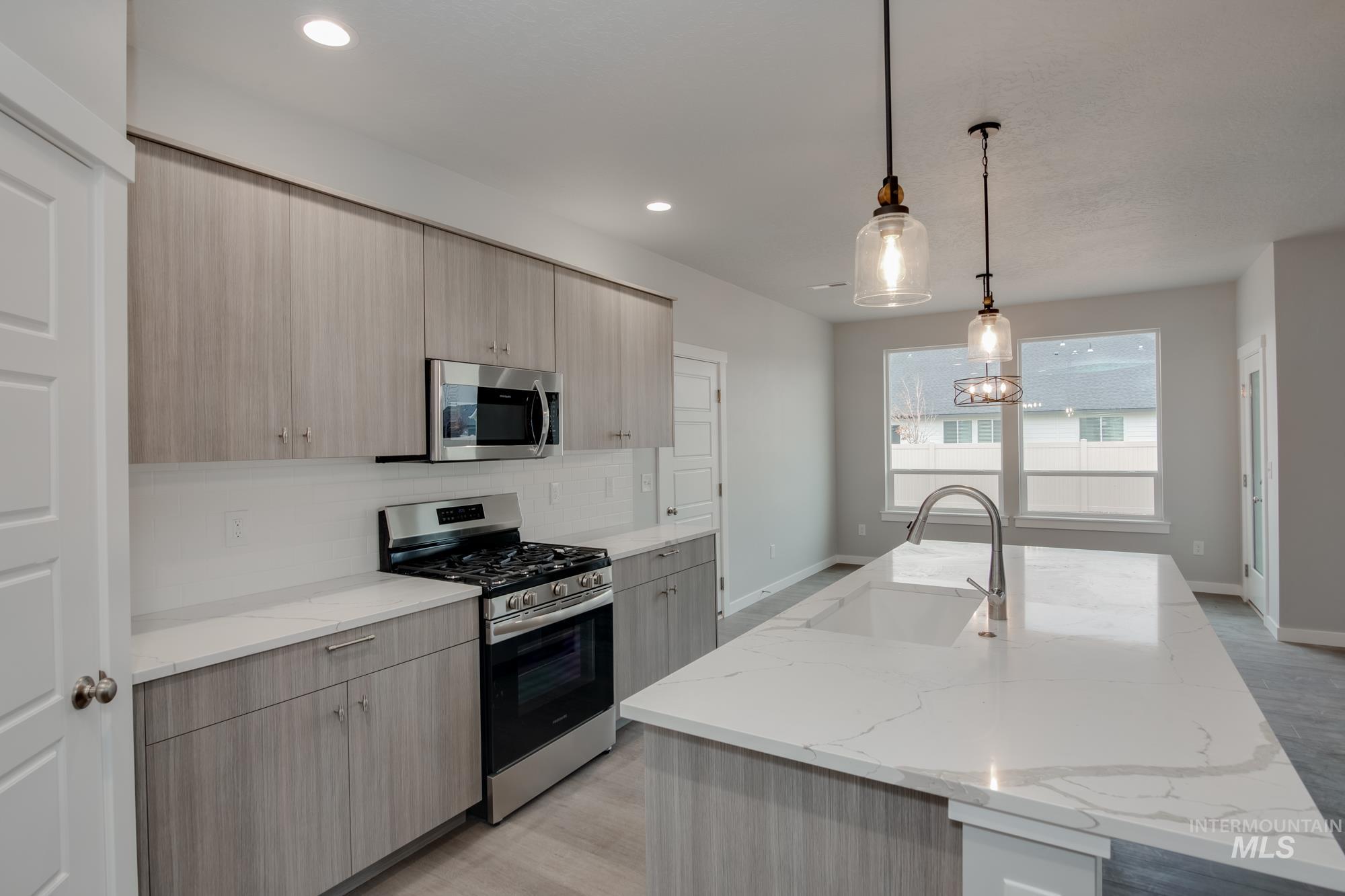 Kitchen featuring stainless steel appliances, light brown cabinetry, decorative backsplash, modern cabinets, and pendant lighting