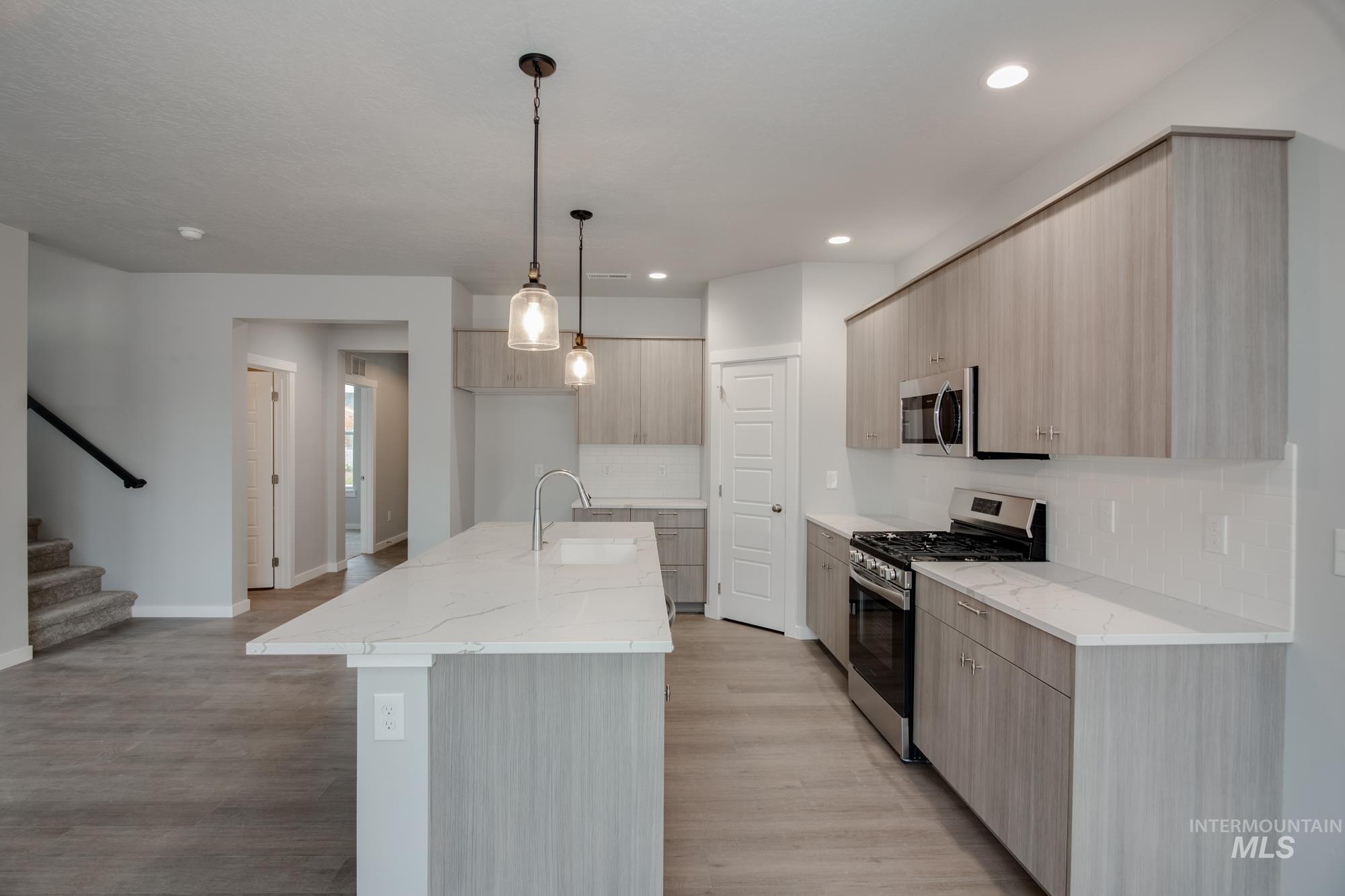 Kitchen featuring appliances with stainless steel finishes, light brown cabinetry, light stone counters, decorative light fixtures, and modern cabinets