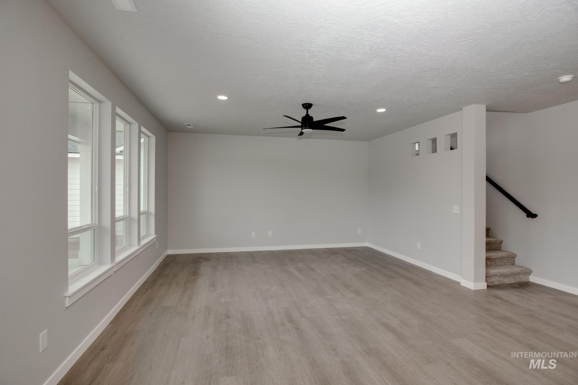 Empty room featuring light wood-type flooring, a ceiling fan, recessed lighting, a textured ceiling, and stairs
