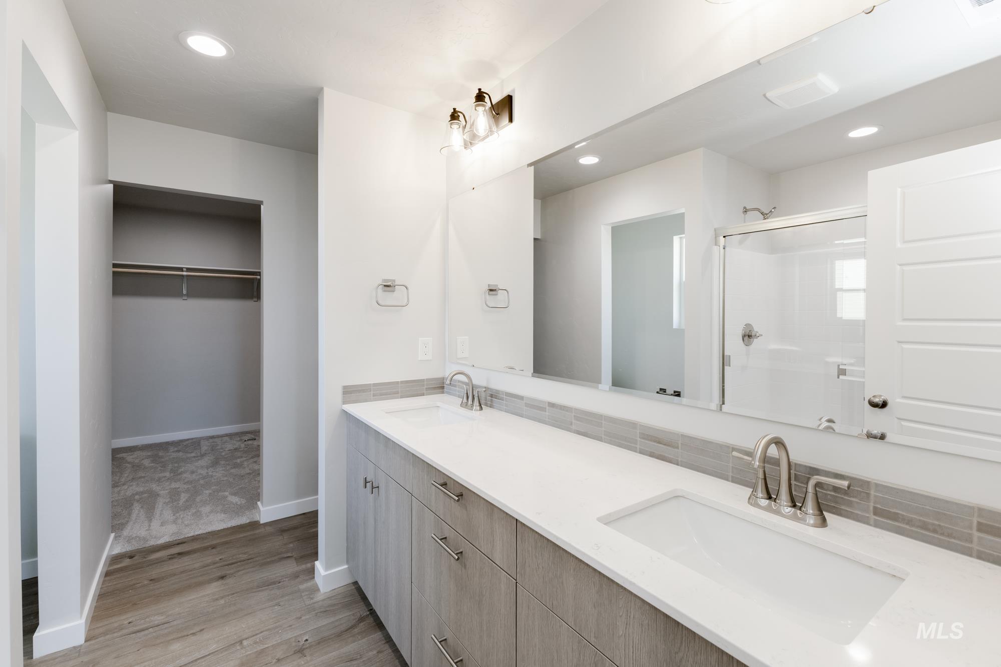 Full bath featuring a spacious closet, double vanity, recessed lighting, light wood-style flooring, and a shower stall