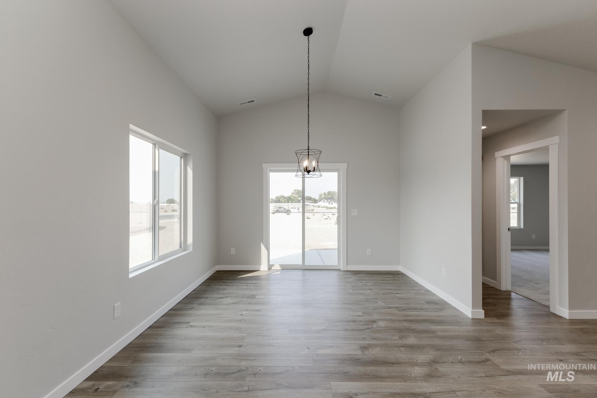 Unfurnished dining area with plenty of natural light, lofted ceiling, a chandelier, and wood finished floors