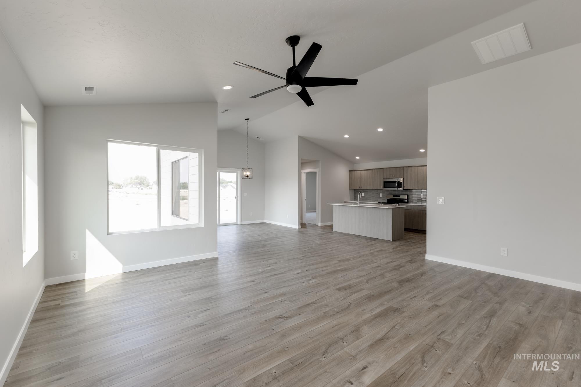 Unfurnished living room featuring a ceiling fan, light wood finished floors, vaulted ceiling, and recessed lighting