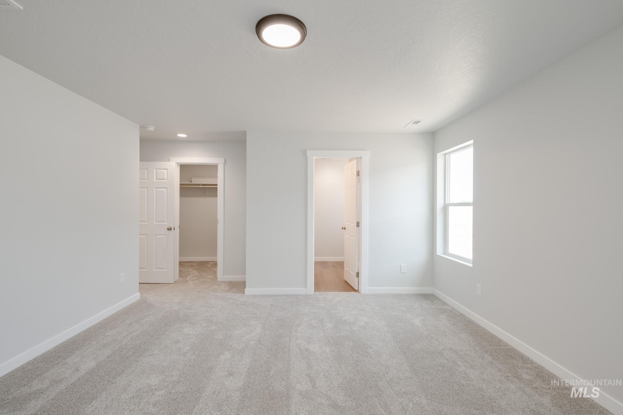 Unfurnished bedroom with a walk in closet, light colored carpet, and ensuite bath