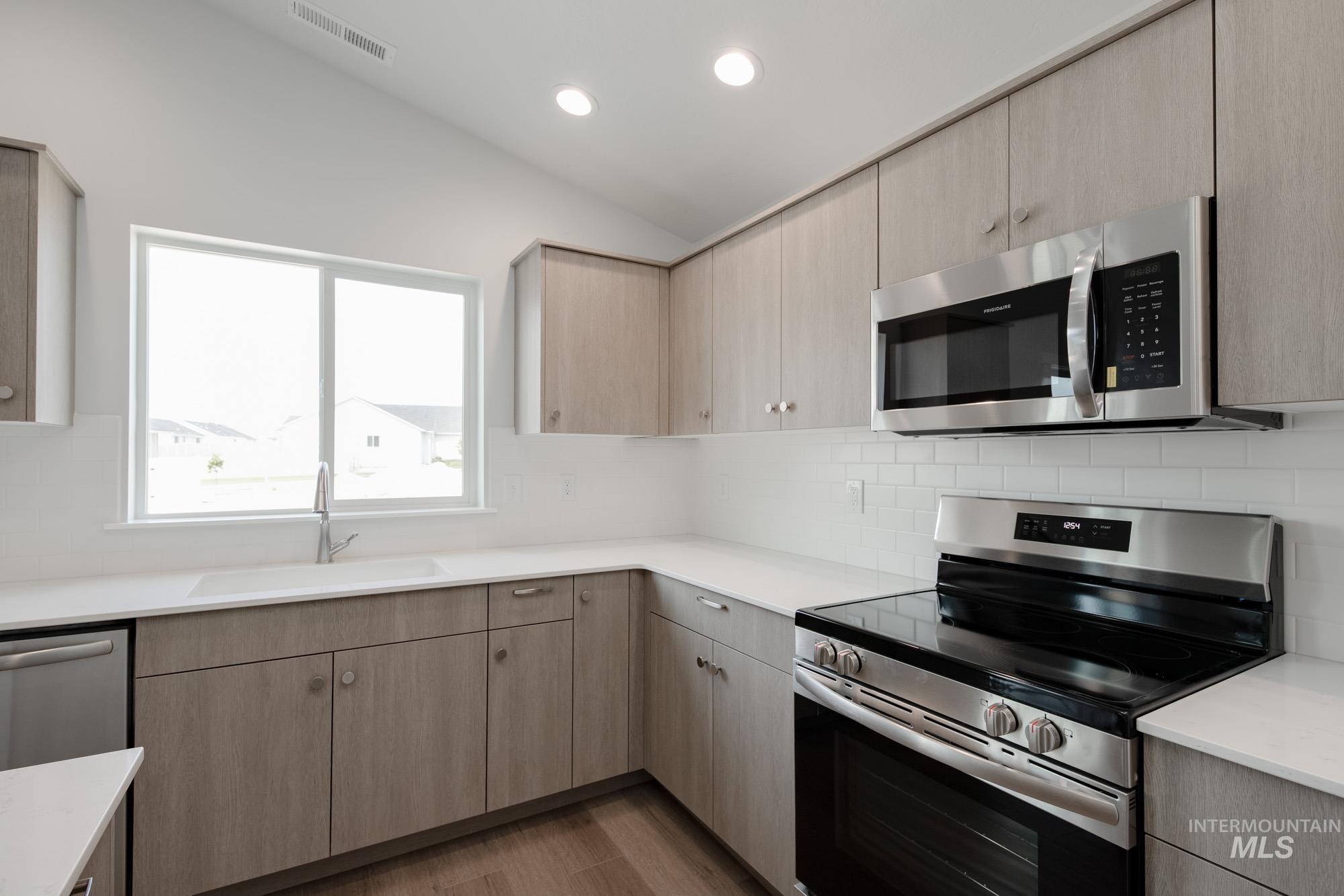 Kitchen featuring stainless steel appliances, light brown cabinetry, decorative backsplash, lofted ceiling, and recessed lighting