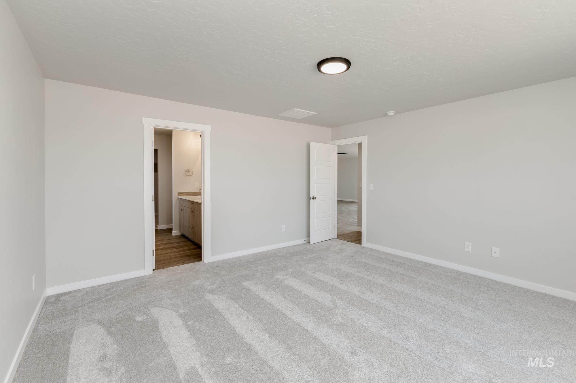 Unfurnished bedroom with light carpet, connected bathroom, and a textured ceiling
