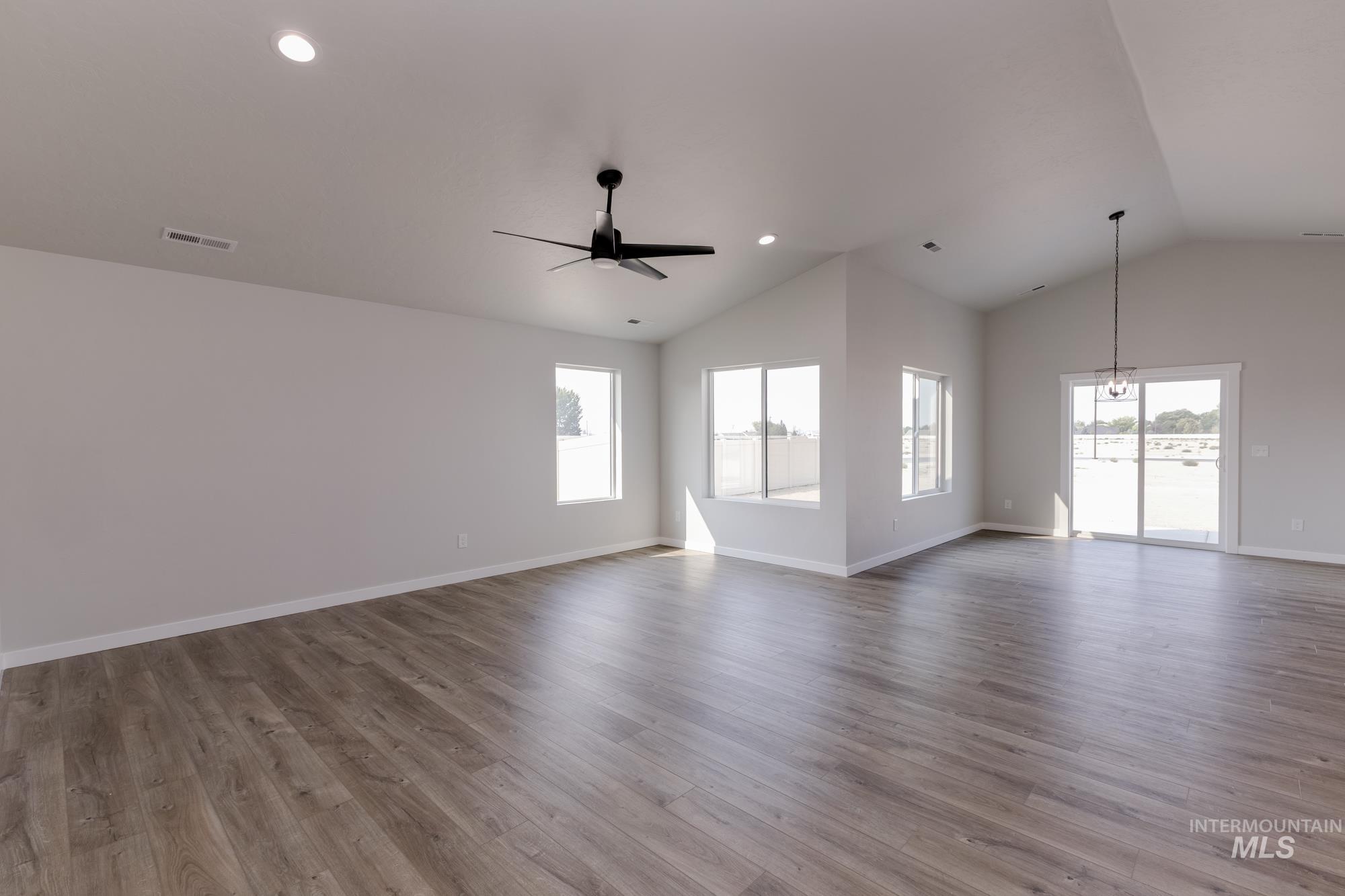 Unfurnished living room featuring healthy amount of natural light, light wood-style floors, ceiling fan, recessed lighting, and high vaulted ceiling