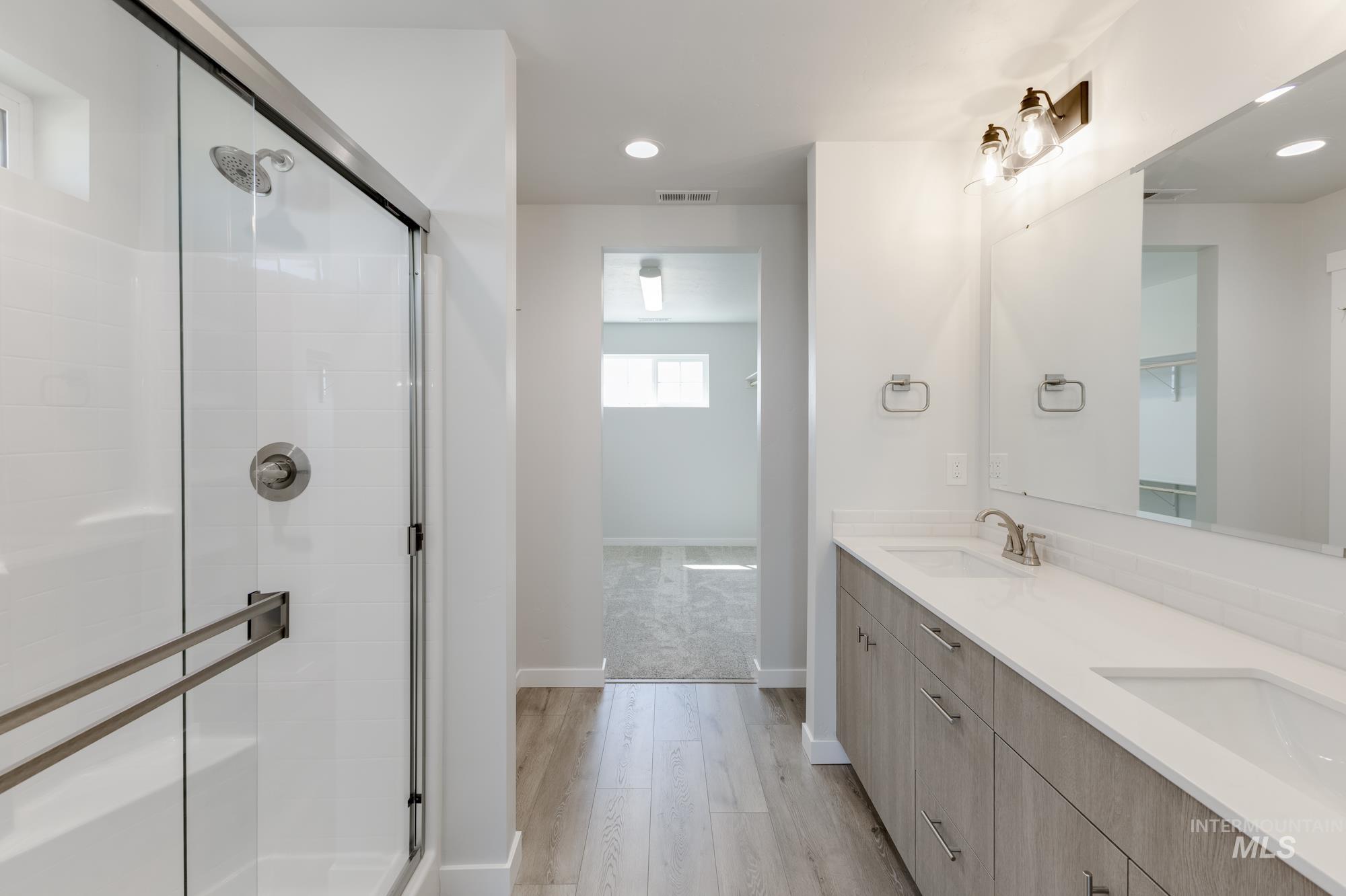Bathroom featuring a stall shower, double vanity, recessed lighting, and light wood-type flooring