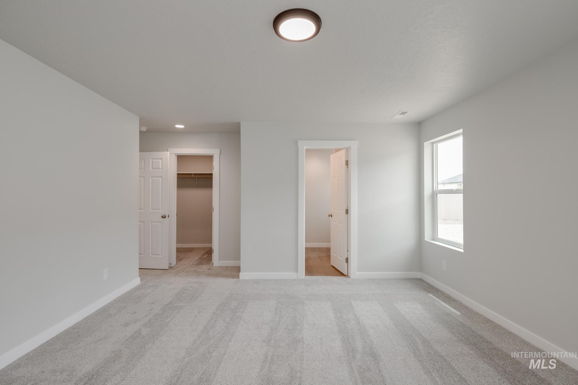 Unfurnished bedroom with light carpet, a walk in closet, connected bathroom, and recessed lighting