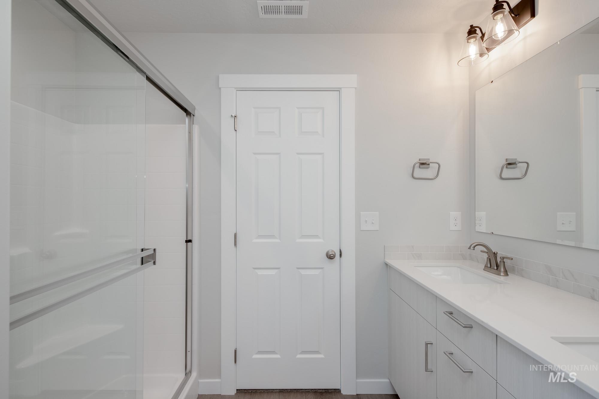 Bathroom featuring double vanity, a stall shower, and dark wood-type flooring