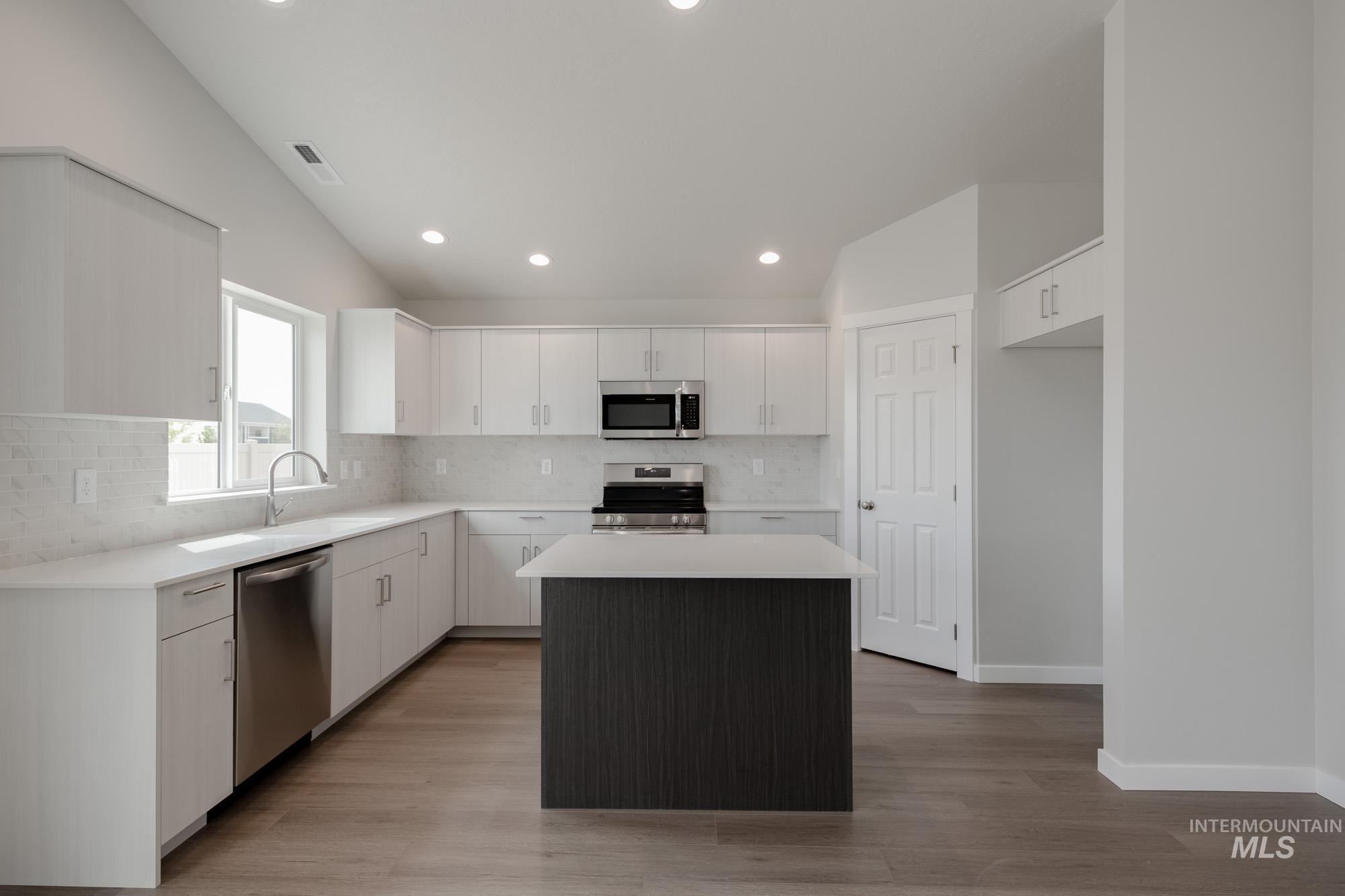 Kitchen featuring a kitchen island, backsplash, white cabinets, stainless steel appliances, and recessed lighting