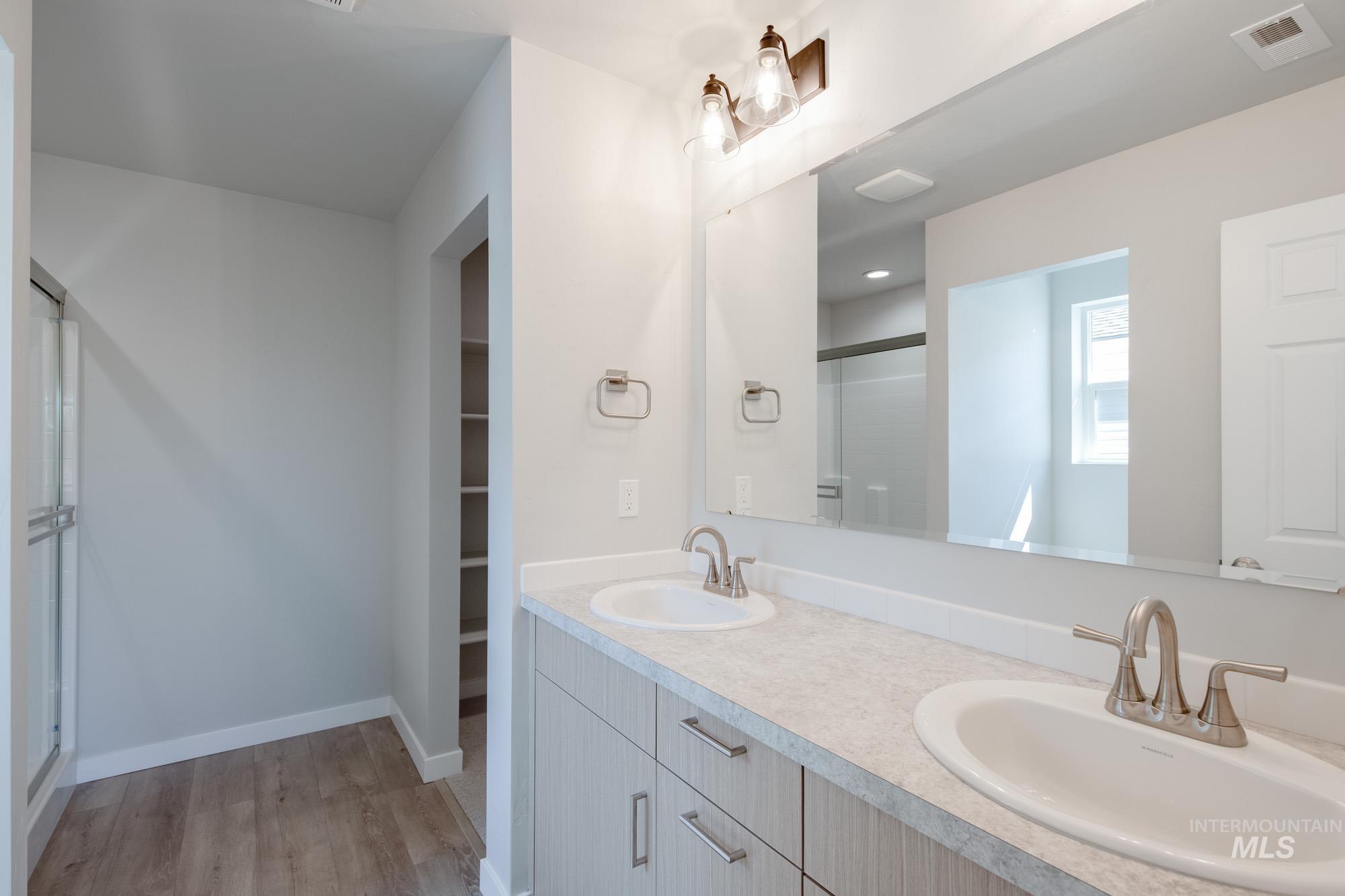 Bathroom with a shower stall, double vanity, light wood-type flooring, and a walk in closet