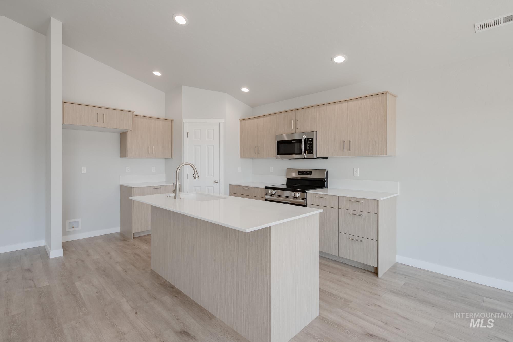 Kitchen with light brown cabinets, appliances with stainless steel finishes, a kitchen island with sink, lofted ceiling, and light wood-style flooring