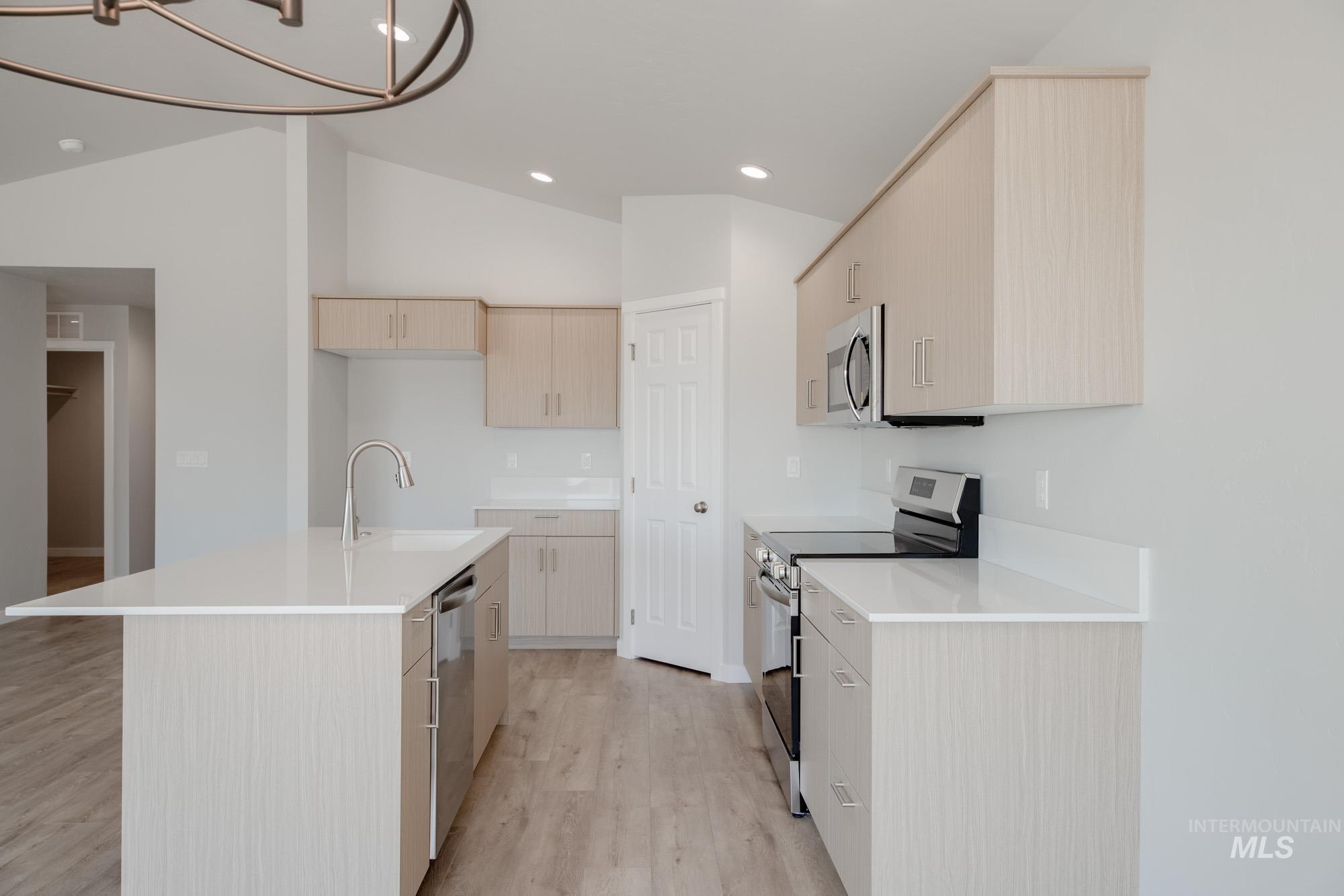 Kitchen featuring light brown cabinets, appliances with stainless steel finishes, modern cabinets, light wood-style floors, and an island with sink