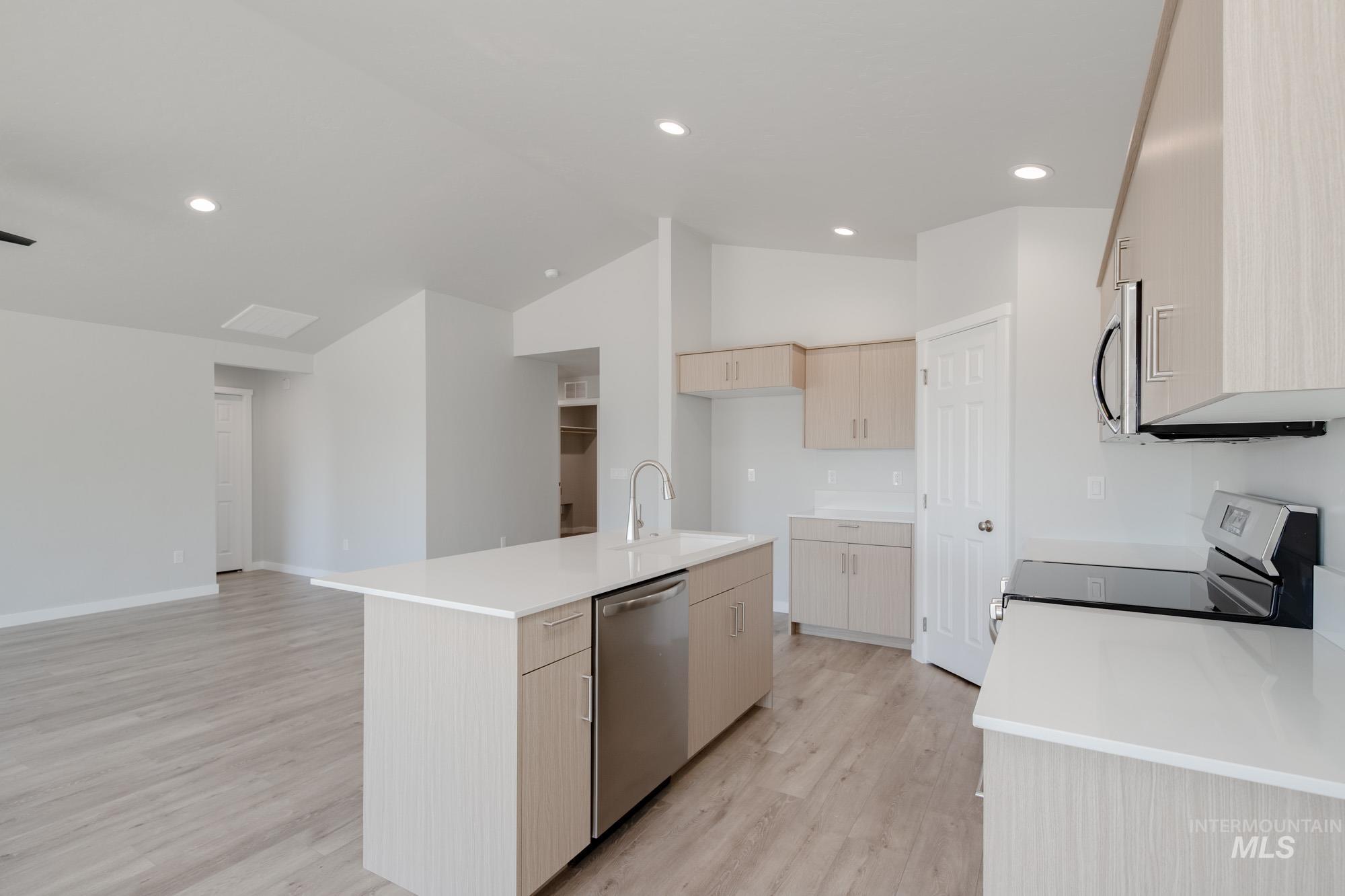 Kitchen with light brown cabinetry, light wood-style flooring, appliances with stainless steel finishes, recessed lighting, and an island with sink