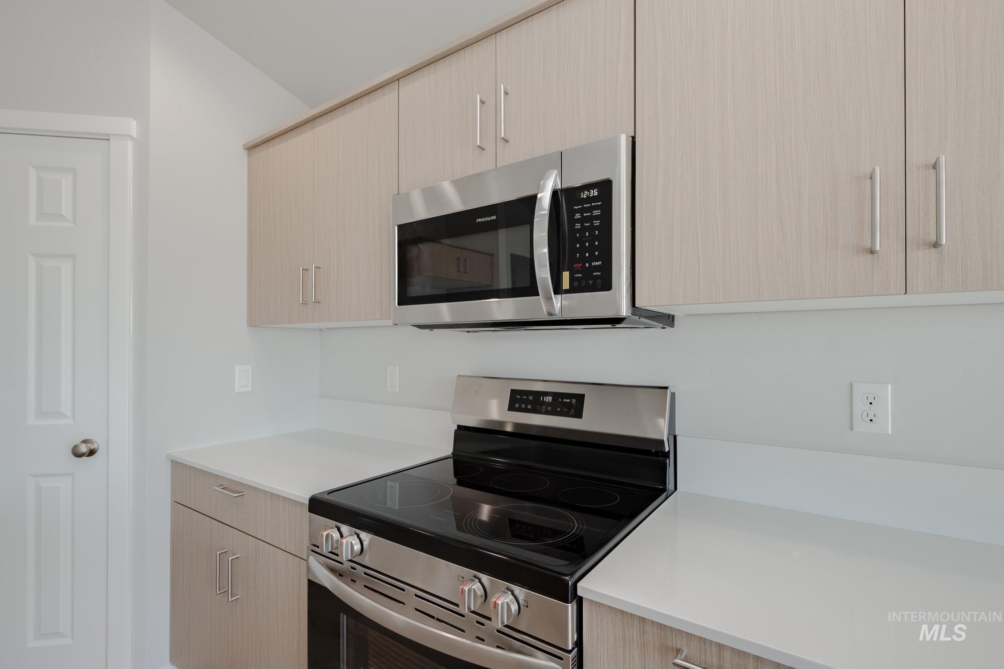 Kitchen with appliances with stainless steel finishes, light brown cabinetry, modern cabinets, and light stone counters