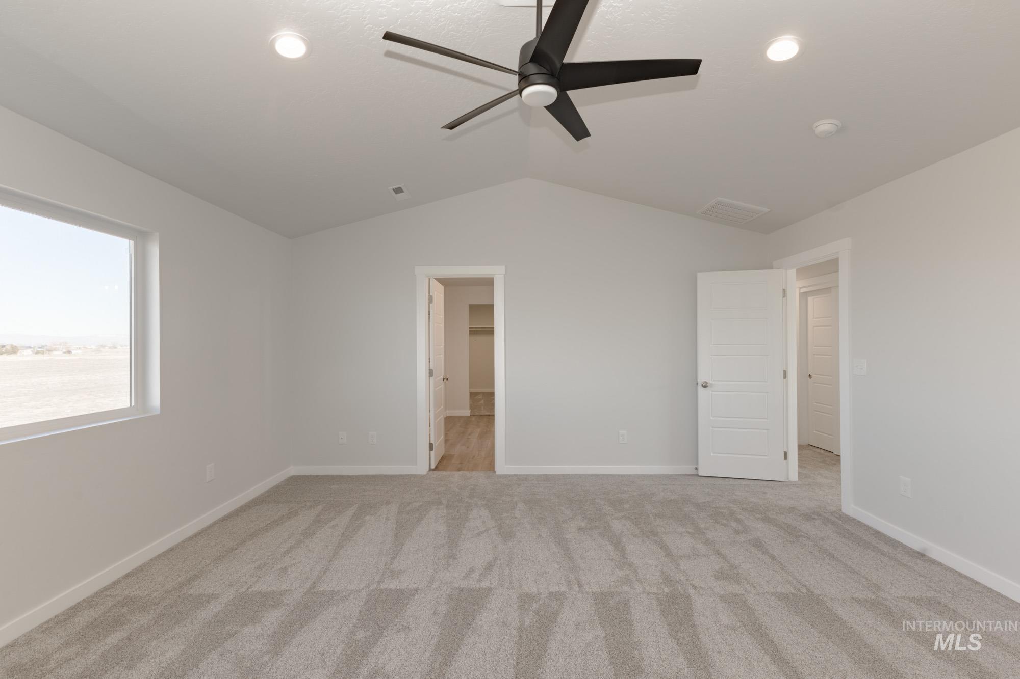 Unfurnished bedroom featuring lofted ceiling, light colored carpet, ceiling fan, and ensuite bathroom