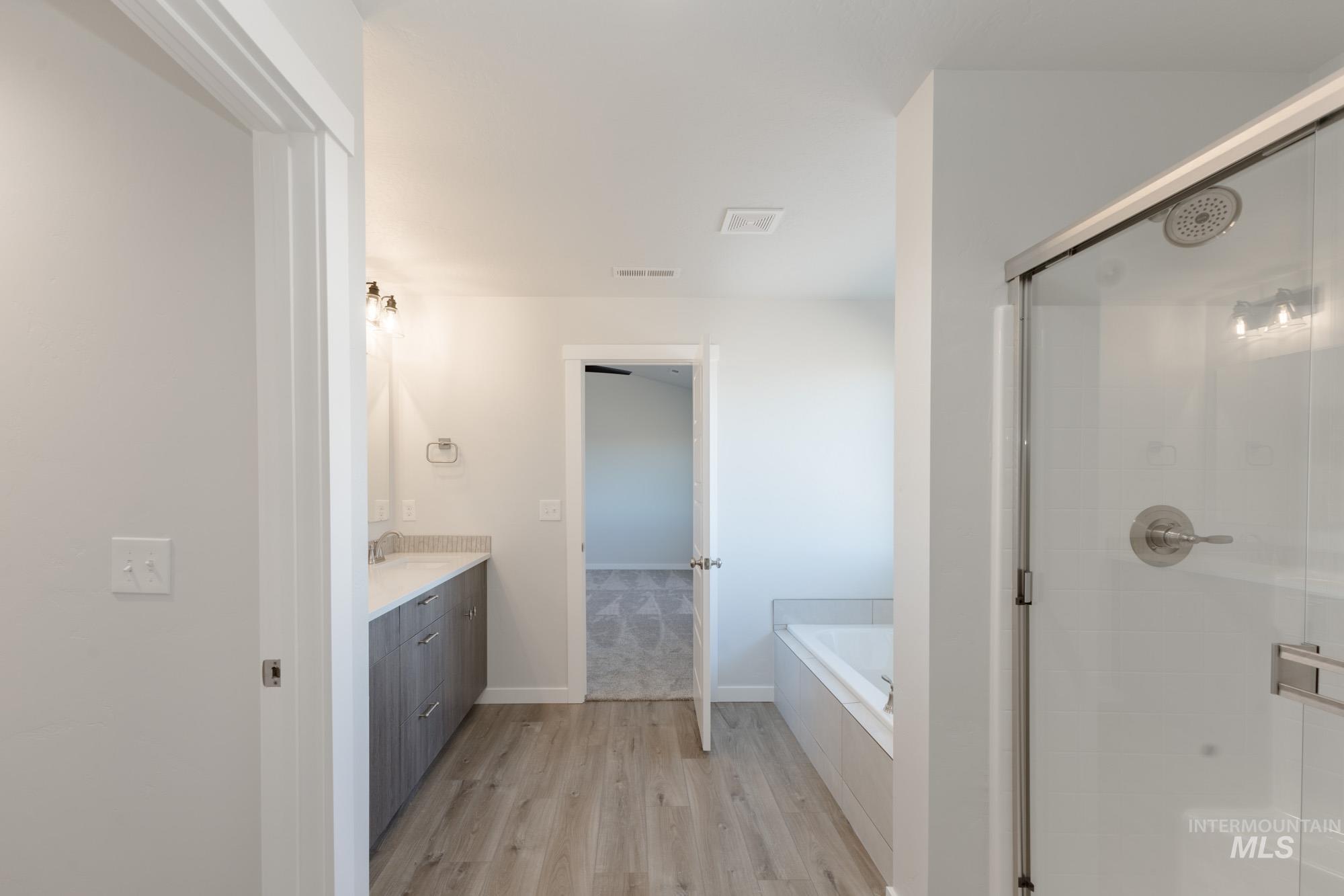 Bathroom featuring vanity, a stall shower, light wood finished floors, and a garden tub
