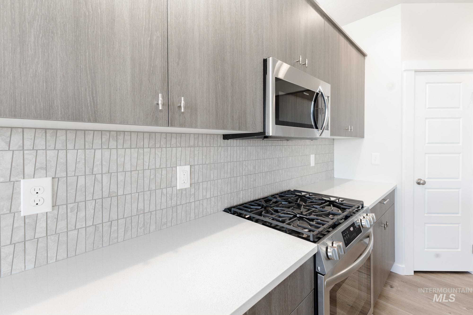 Kitchen with stainless steel appliances, modern cabinets, light wood finished floors, and backsplash