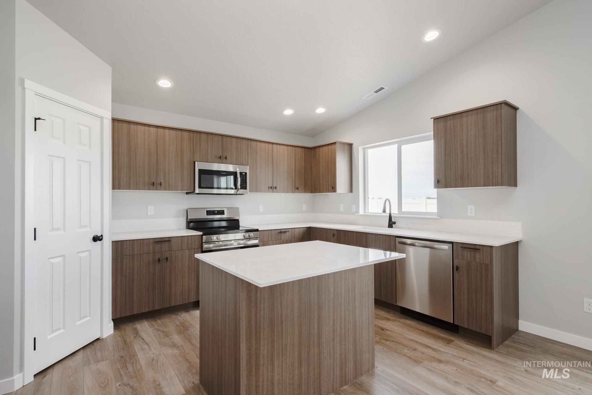 Kitchen with stainless steel appliances, light wood-type flooring, modern cabinets, recessed lighting, and lofted ceiling
