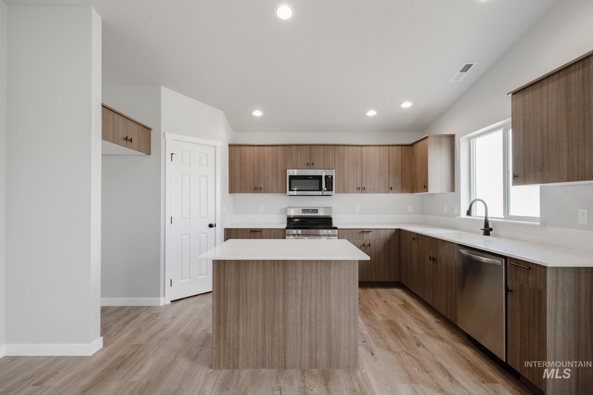 Kitchen with modern cabinets, a center island, appliances with stainless steel finishes, recessed lighting, and light wood-style flooring