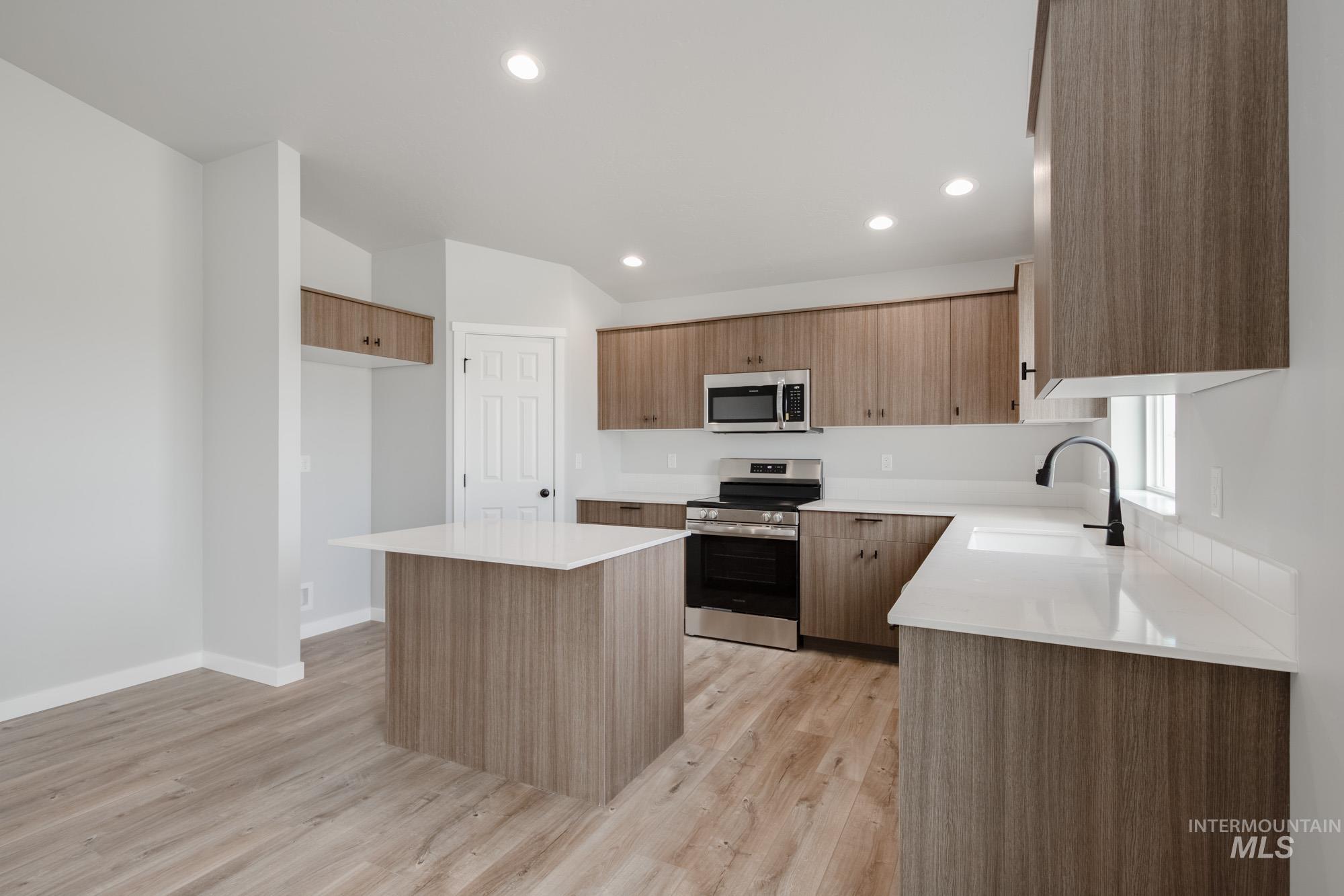 Kitchen with appliances with stainless steel finishes, a kitchen island, light wood-type flooring, modern cabinets, and recessed lighting