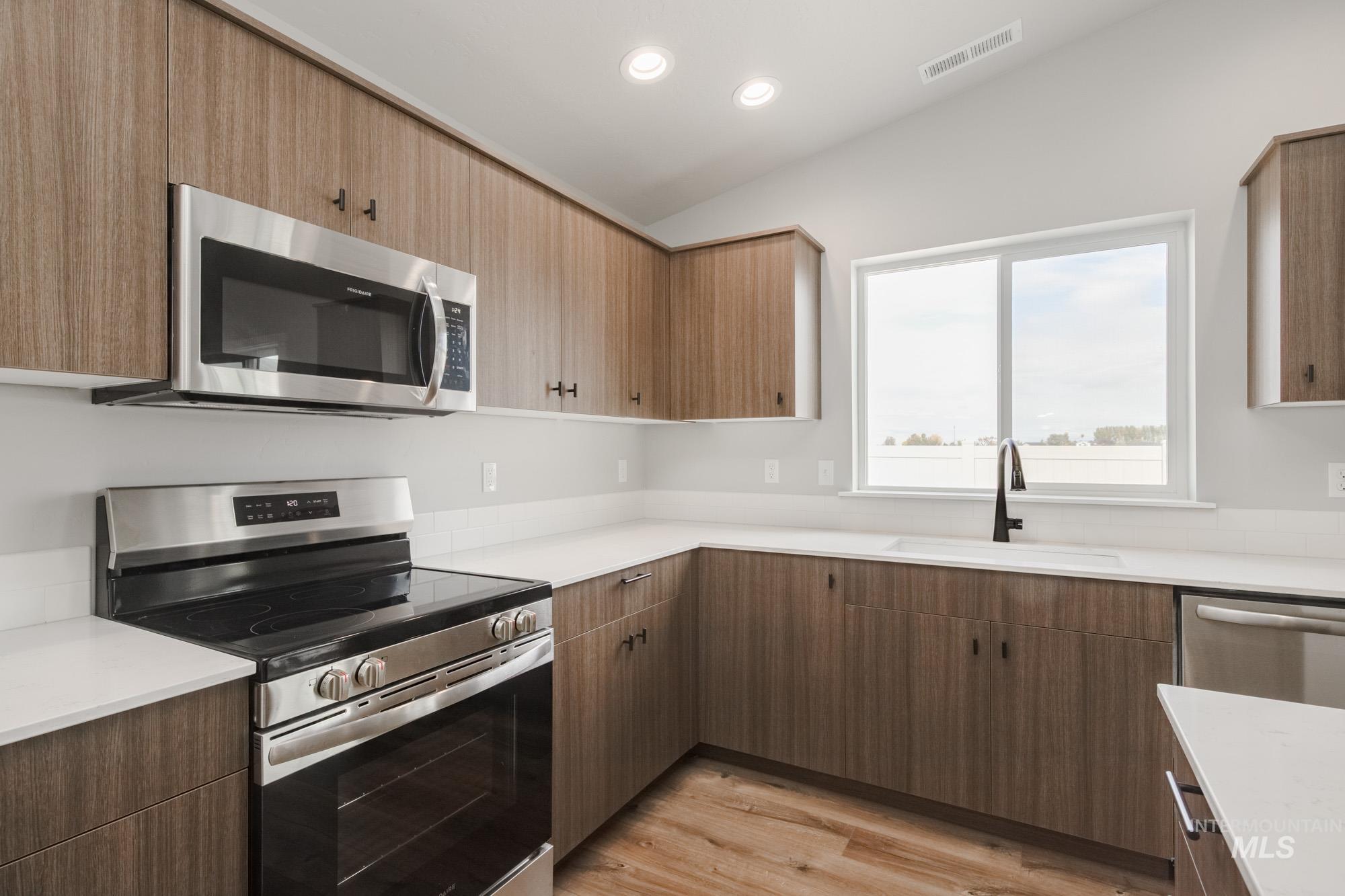 Kitchen featuring appliances with stainless steel finishes, light wood finished floors, recessed lighting, light stone counters, and lofted ceiling