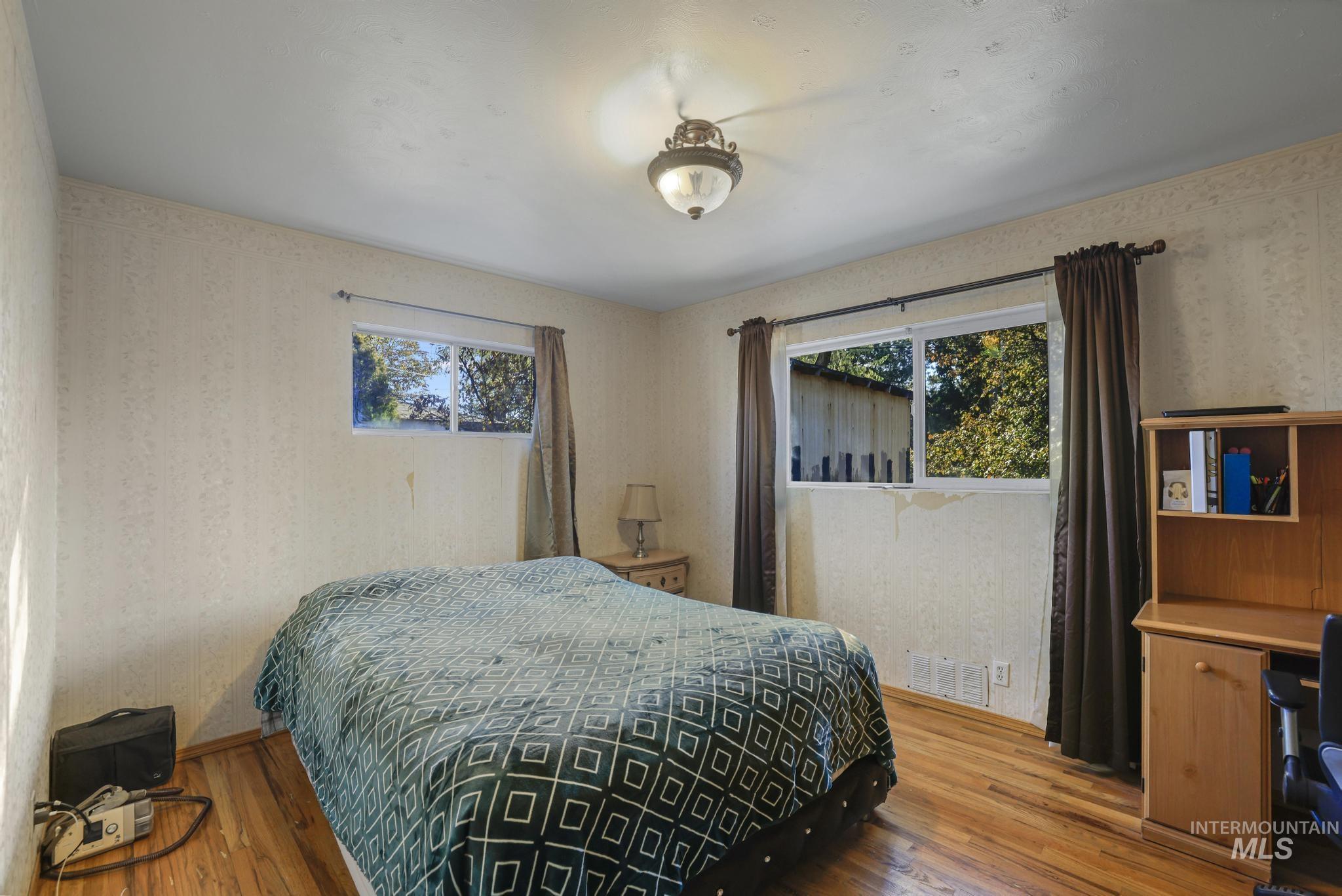 Bedroom featuring wallpapered walls, wood finished floors, and multiple windows