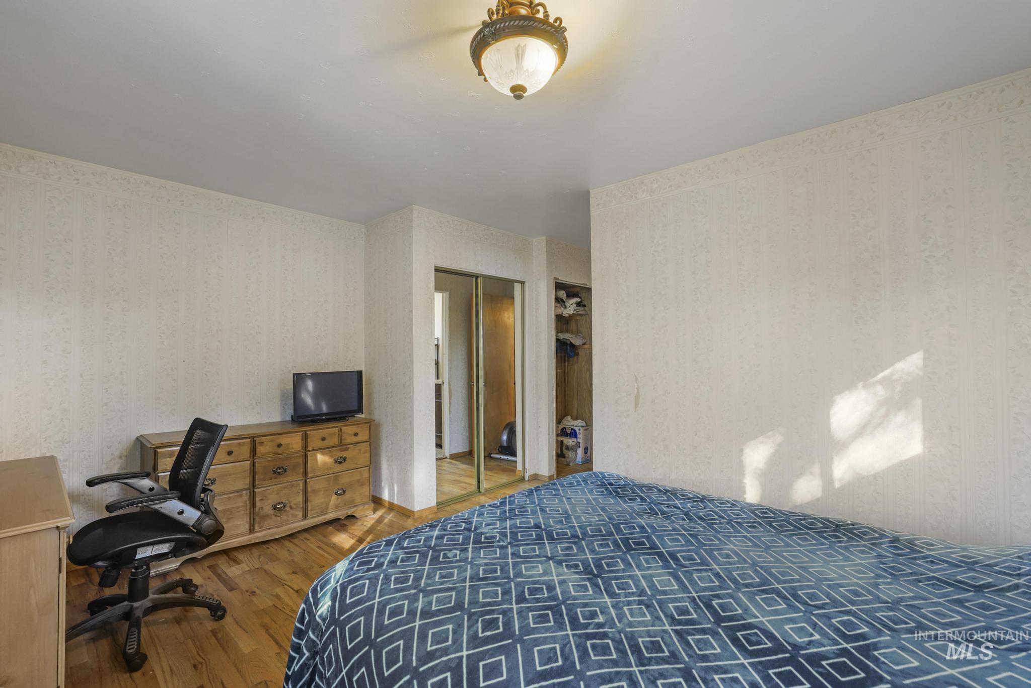 Bedroom with wood finished floors, wallpapered walls, and a desk
