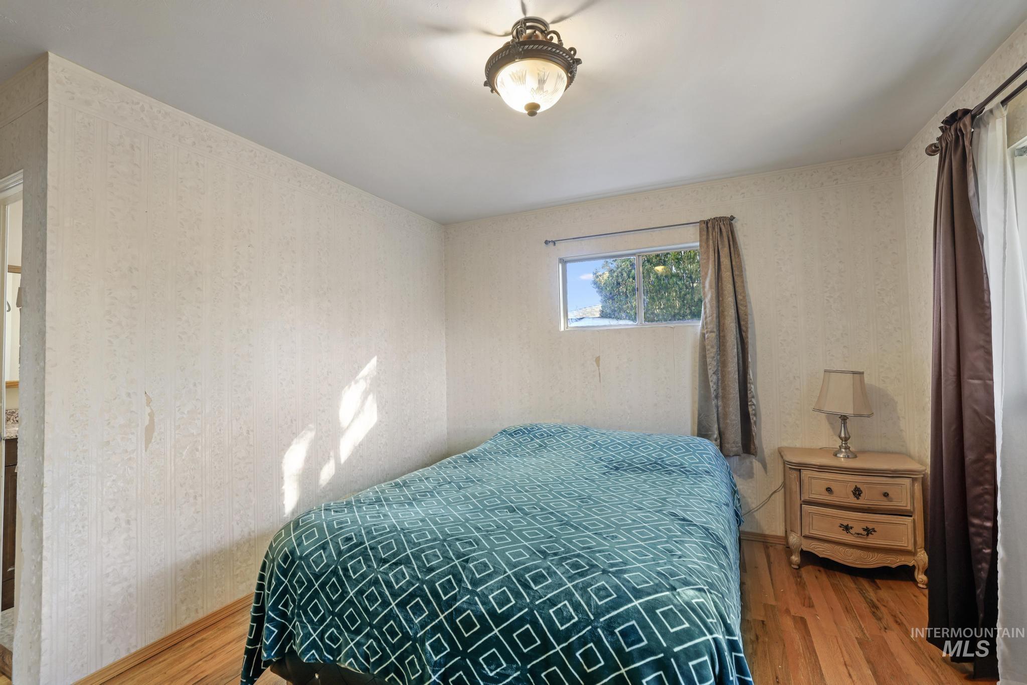 Bedroom with wood finished floors and wallpapered walls