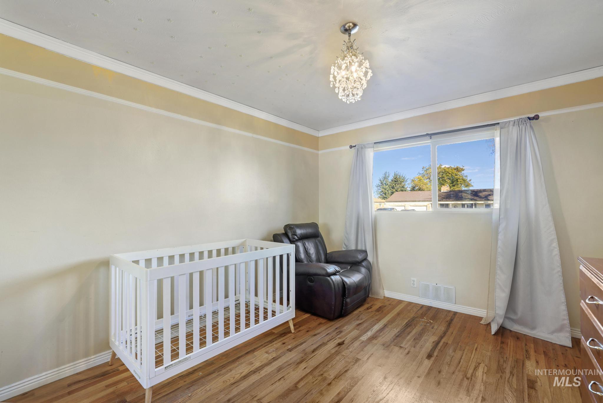 Bedroom with crown molding, wood finished floors, a crib, and a chandelier