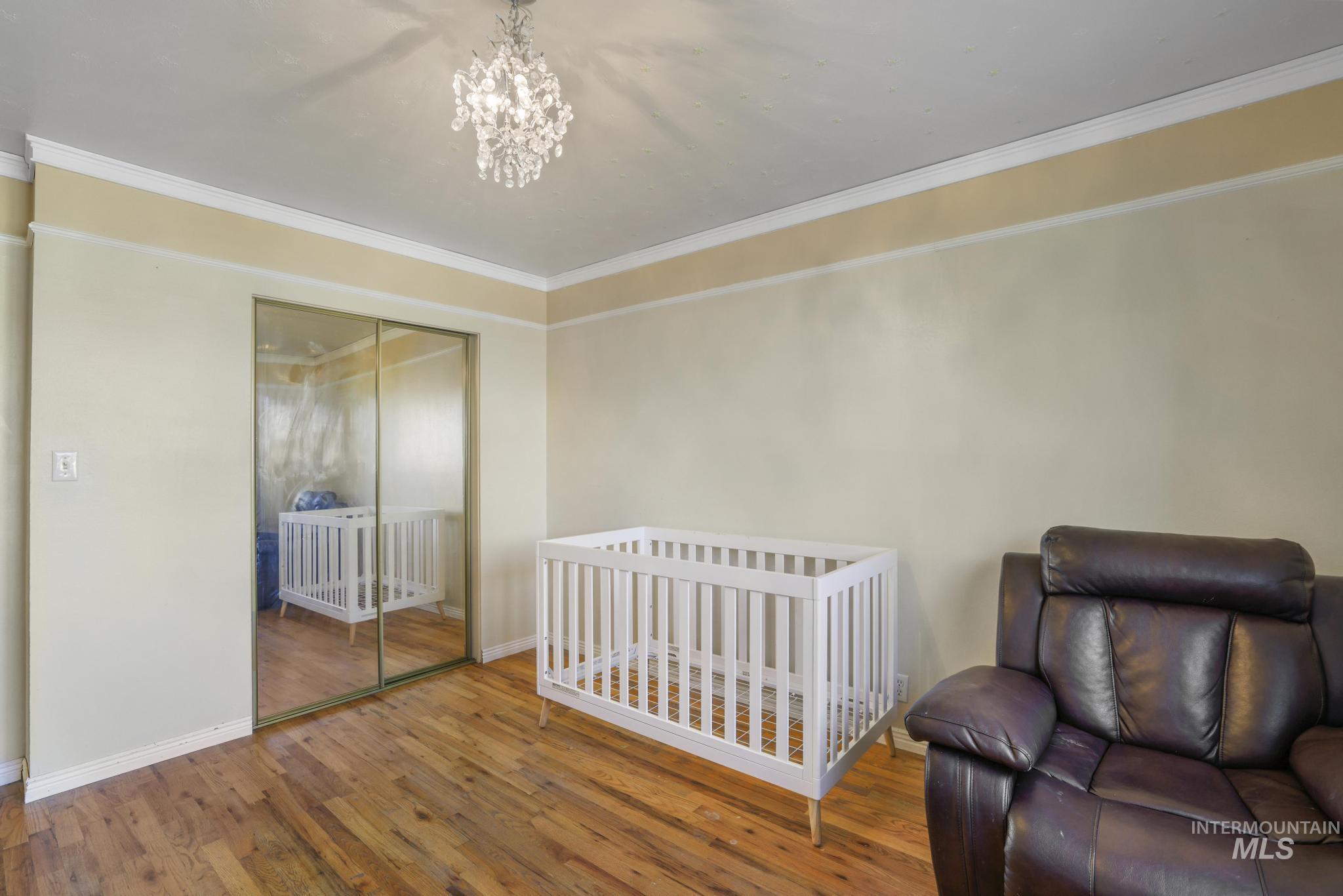 Bedroom with crown molding, wood finished floors, a closet, a crib, and a chandelier