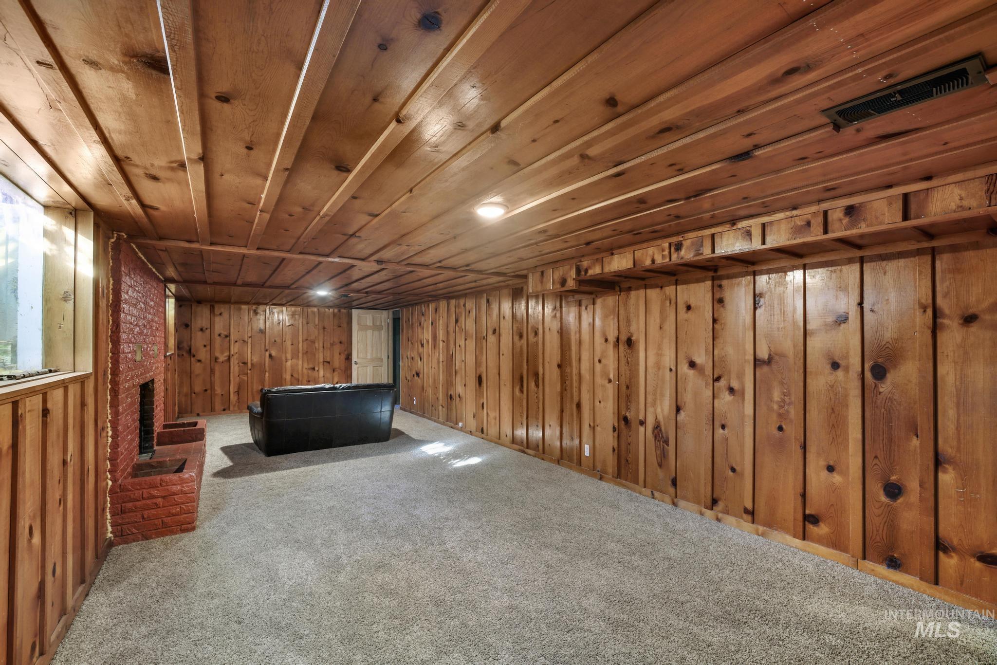 Finished below grade area with carpet flooring, wood ceiling, wood walls, and a brick fireplace