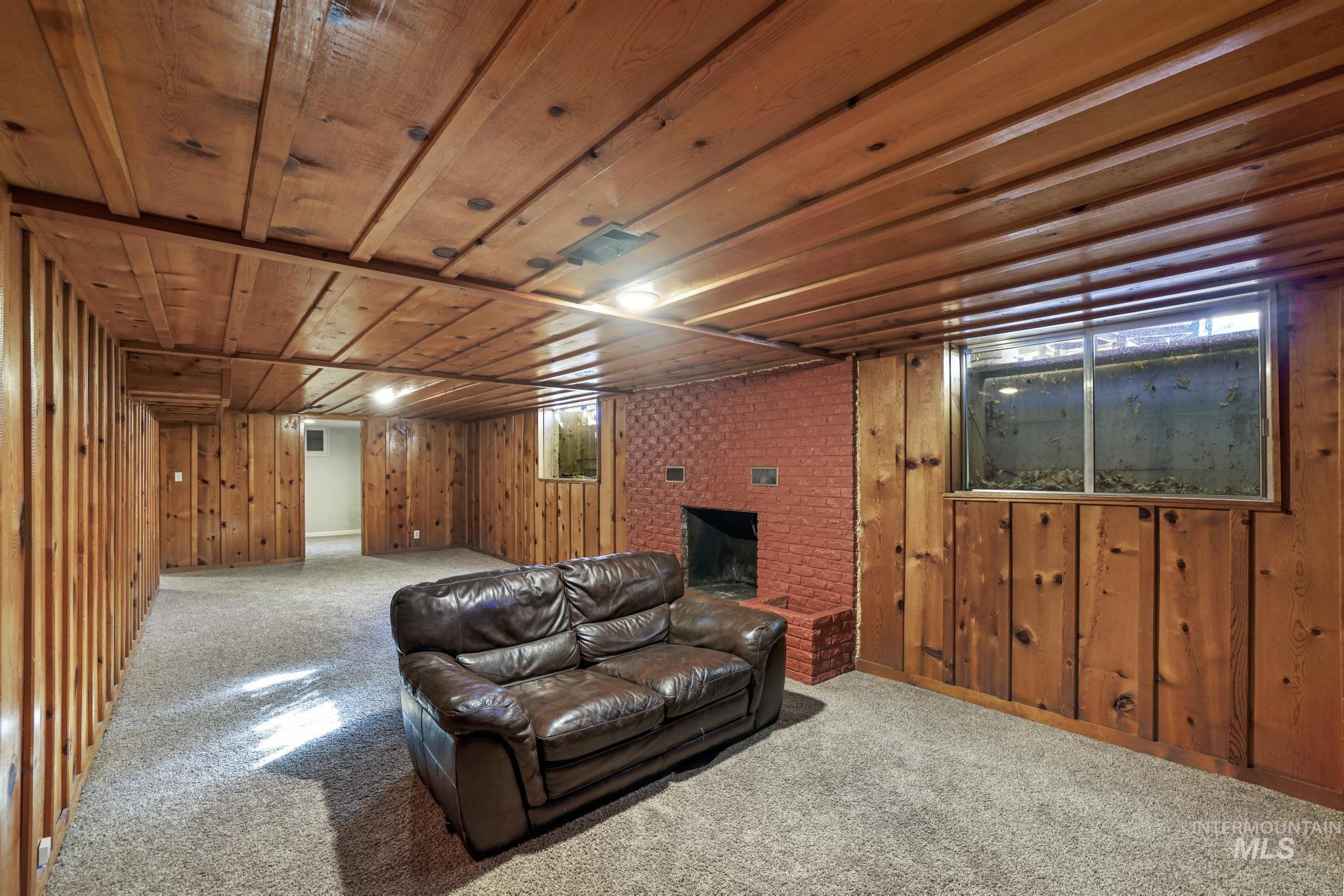 Carpeted living area featuring wood walls, wooden ceiling, and a brick fireplace