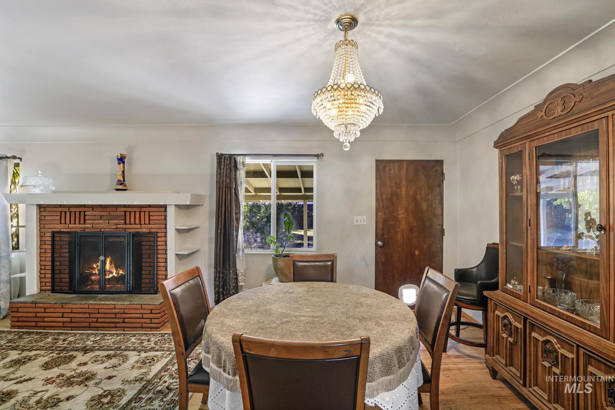 Dining area with wood finished floors, a brick fireplace, and a chandelier
