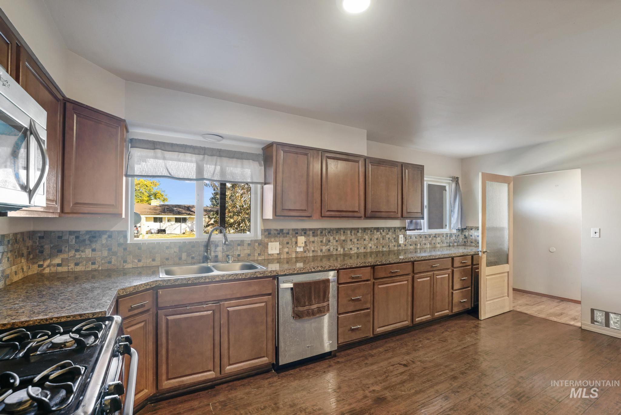 Kitchen featuring dark wood-type flooring, appliances with stainless steel finishes, tasteful backsplash, and brown cabinets