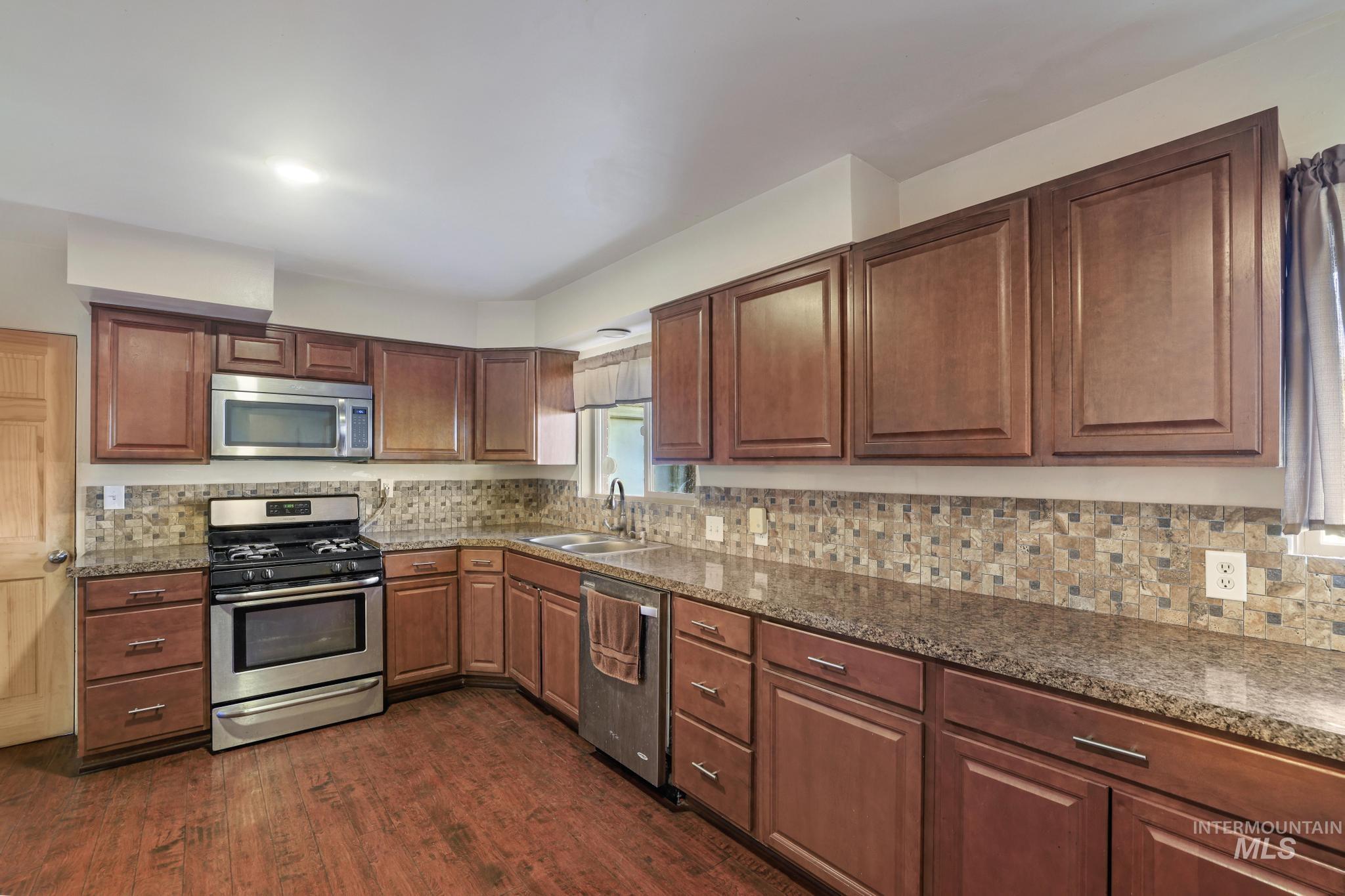 Kitchen featuring appliances with stainless steel finishes, dark stone counters, dark wood-type flooring, and tasteful backsplash
