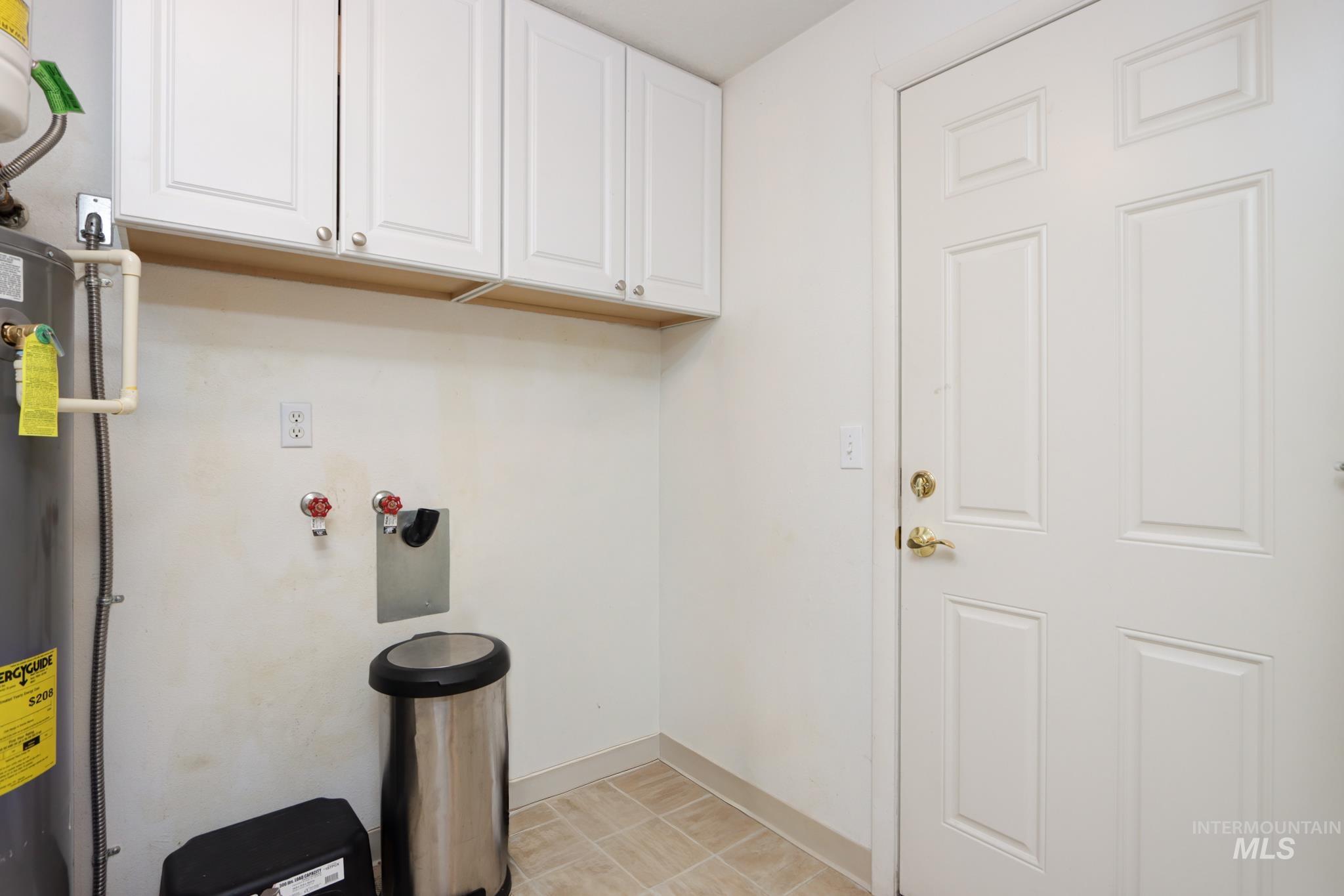 Laundry room with washer hookup, cabinet space, water heater, and light tile patterned floors