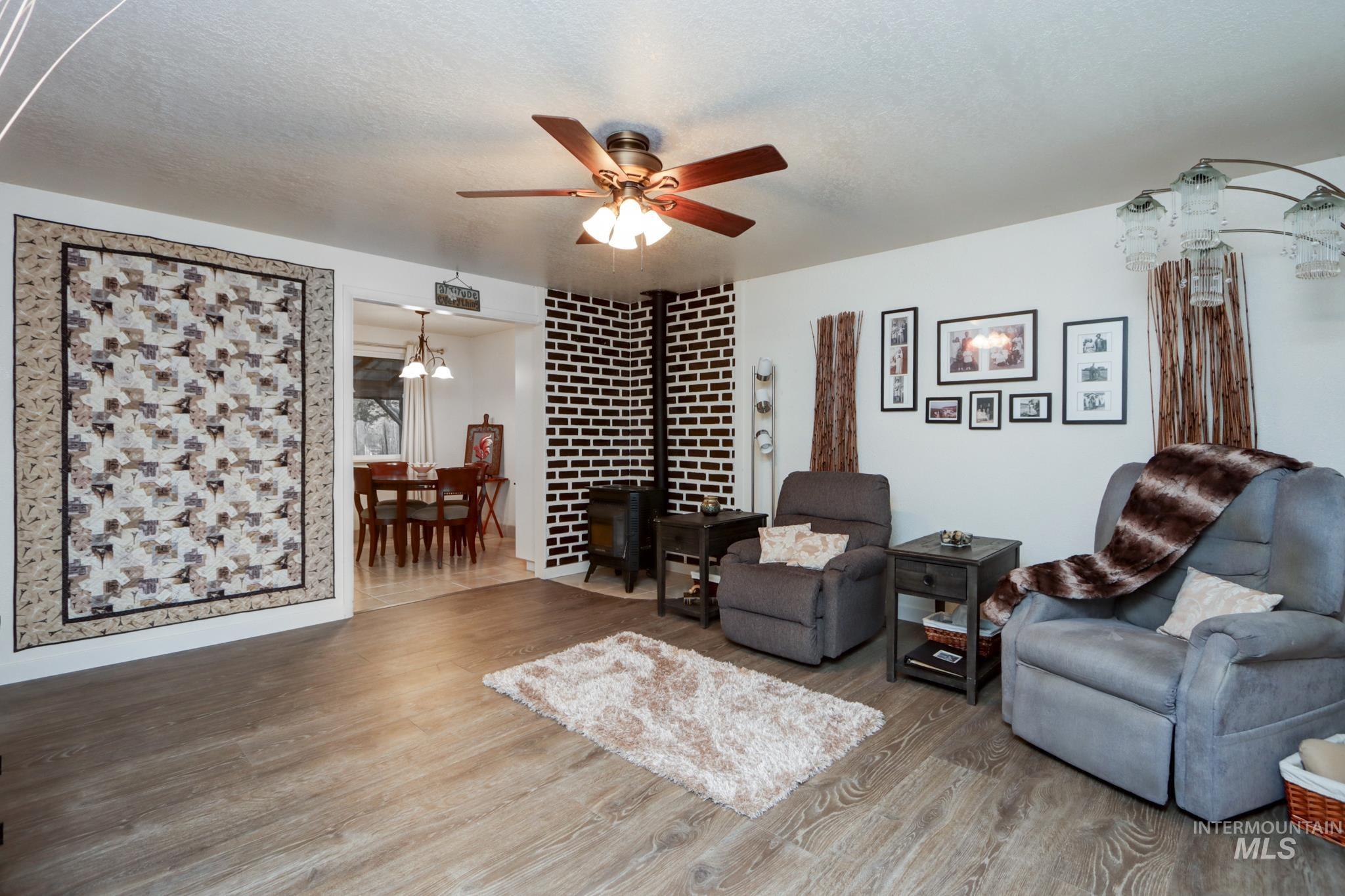 Living area featuring a wood stove, wood finished floors, a ceiling fan, a chandelier, and a textured ceiling